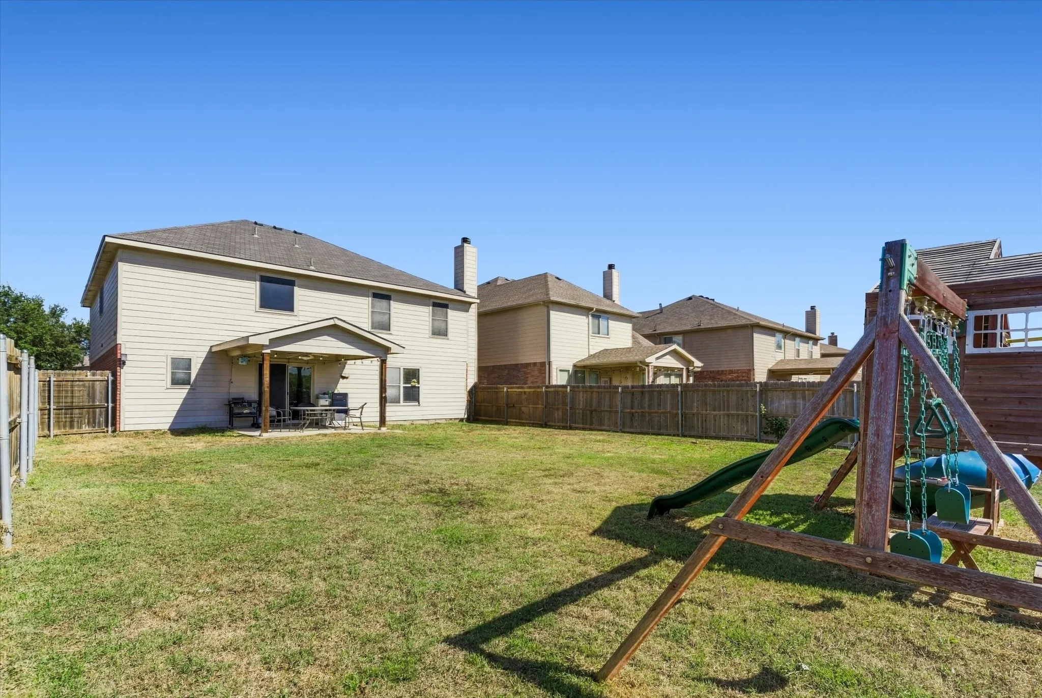 Expansive backyard featuring a covered patio, wood fencing, and a two-story exterior