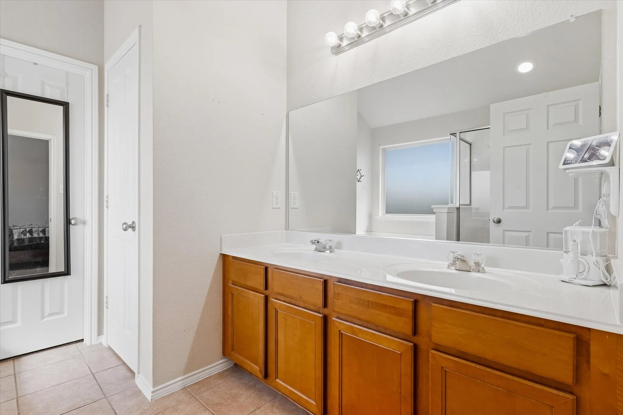 Dual vanity with white countertops, wood-finish cabinetry, and a large wall-mounted mirror