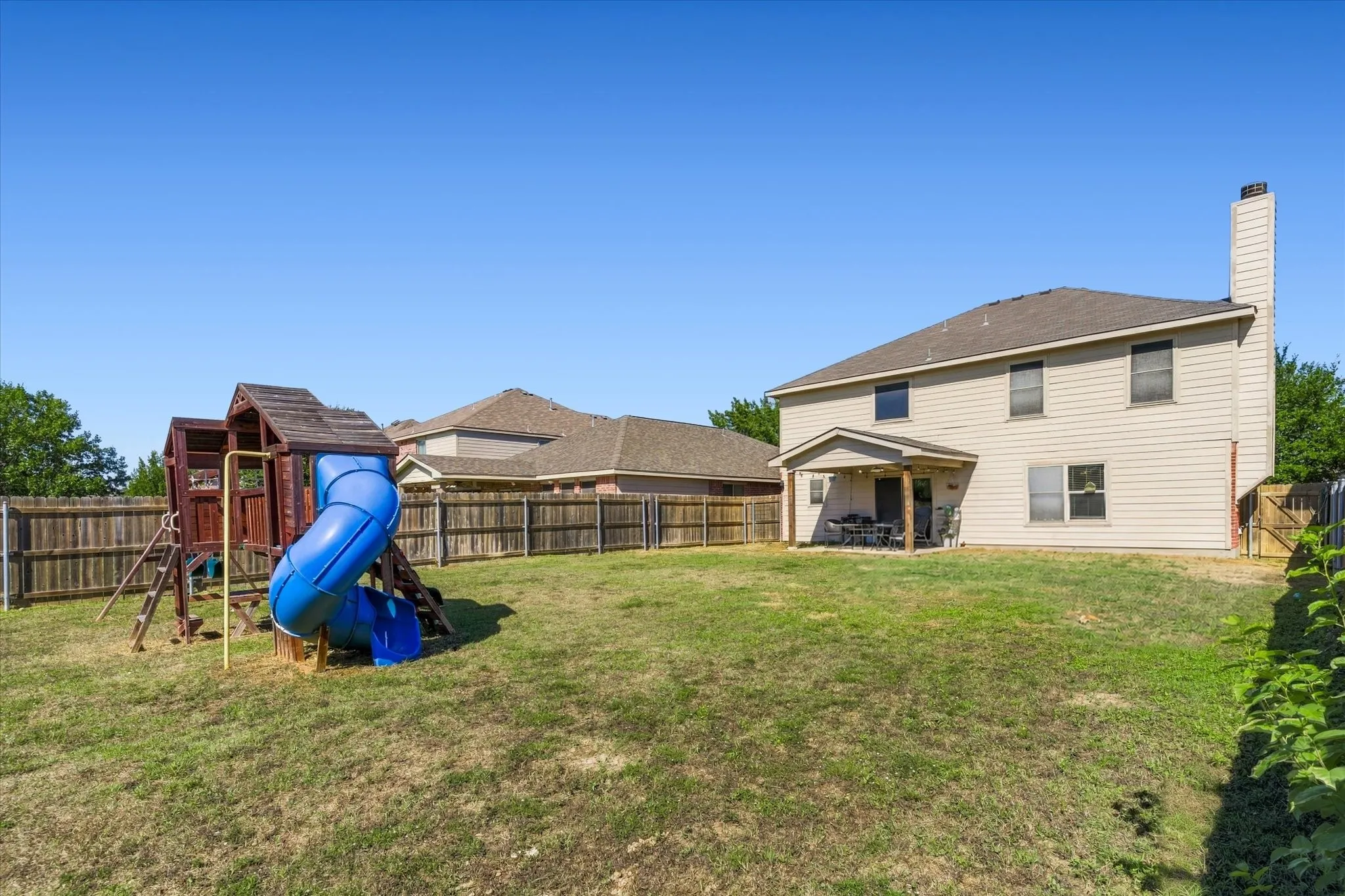 Expansive backyard featuring a covered patio, wood privacy fencing, and a two-story residence with horizontal siding