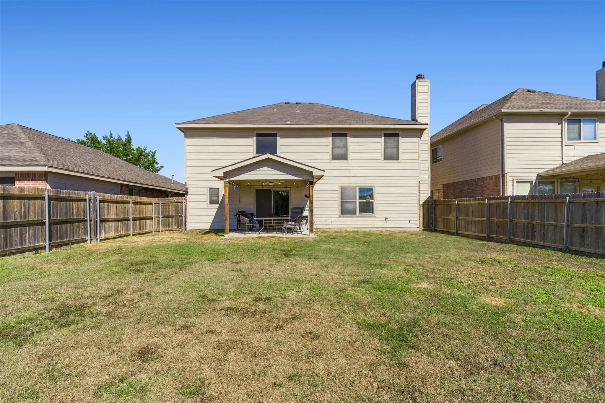 Expansive fenced backyard with a covered patio and a two-story exterior