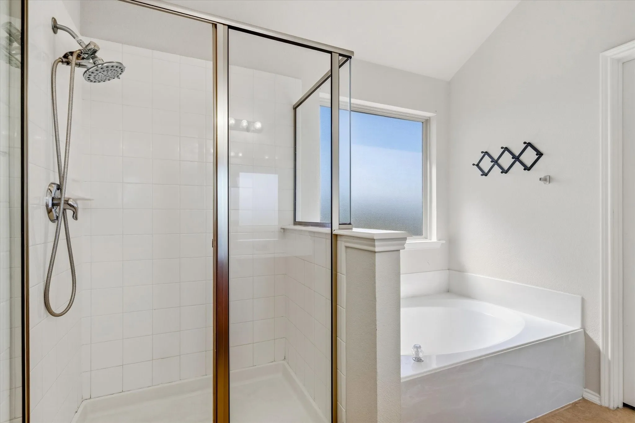 Glass-enclosed shower with brushed nickel fixtures, white tiled walls, built-in corner bathtub, and frosted privacy window
