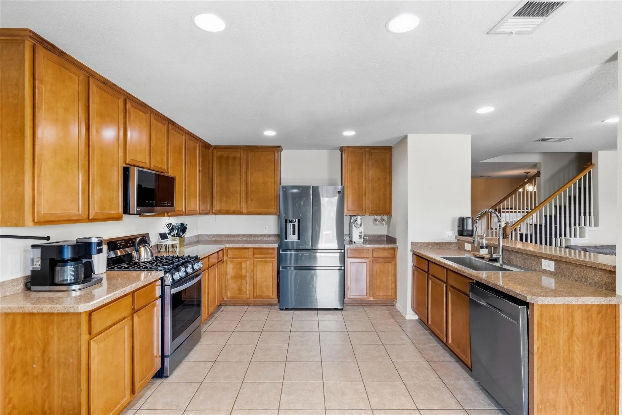 Kitchen featuring wood cabinetry, stone-finish countertops, stainless steel appliances, and tile flooring