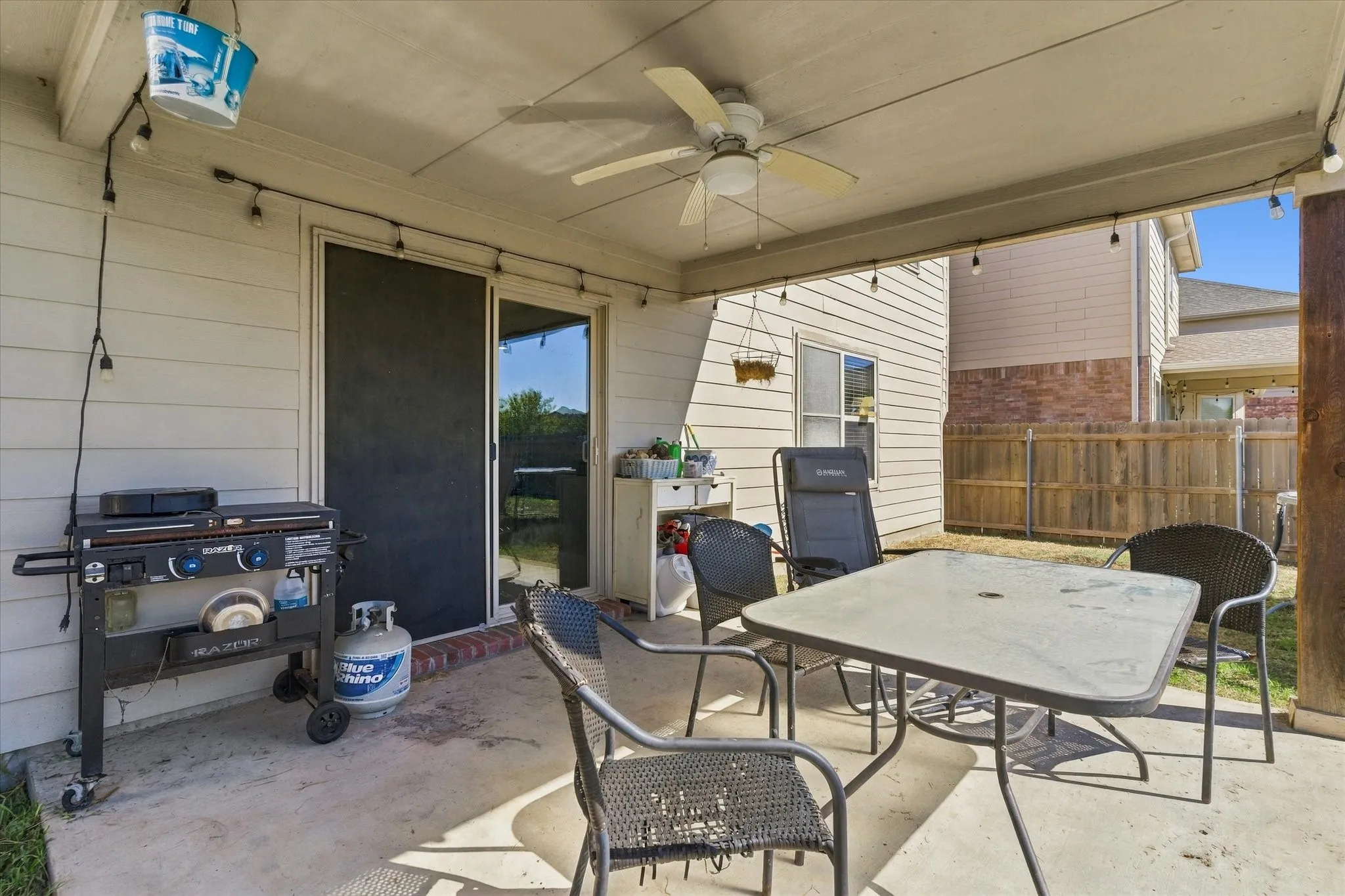 Covered concrete patio with ceiling fan, string lighting, and sliding glass door