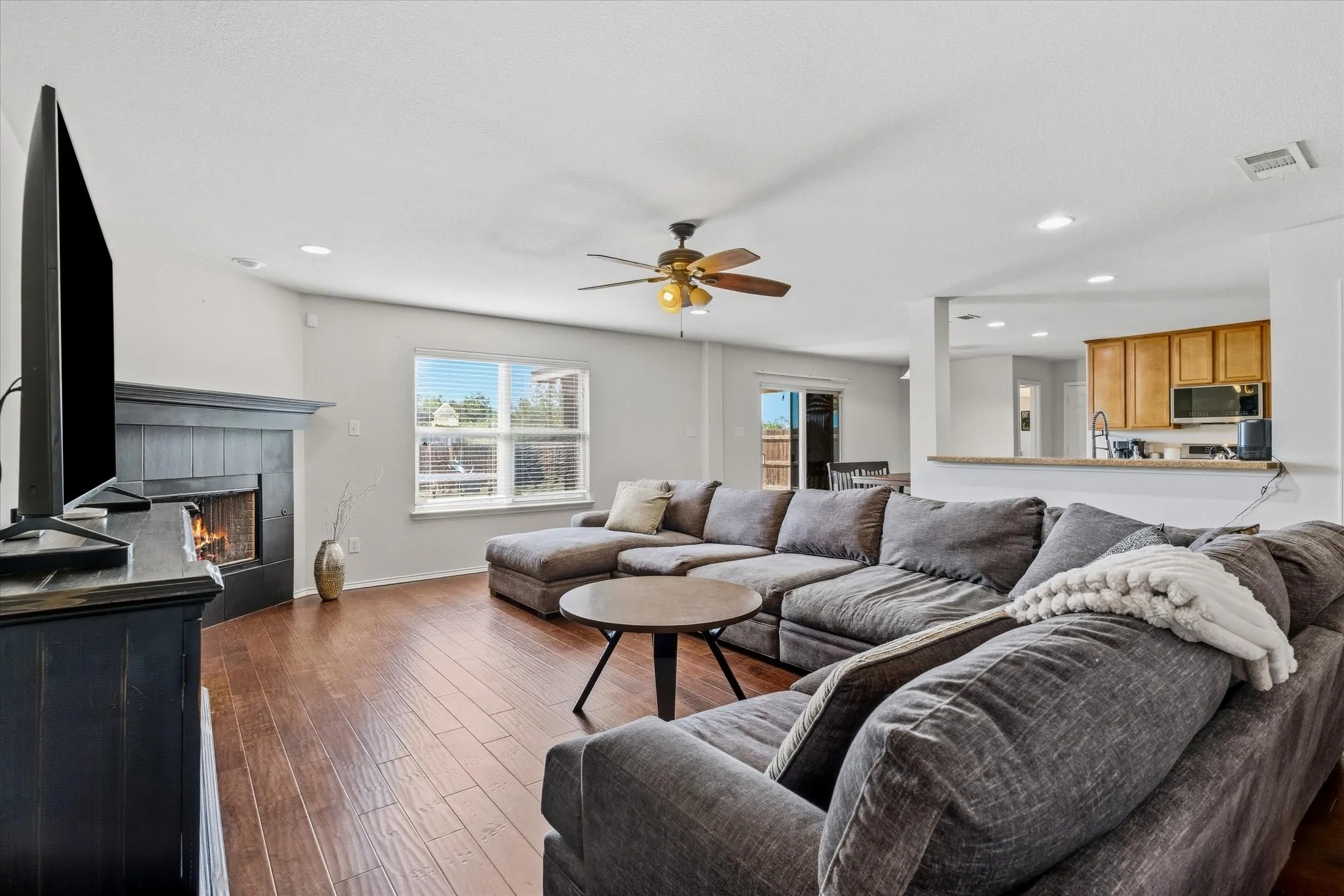 Living area featuring wood-finish flooring, a fireplace with a dark mantel, recessed lighting, and a ceiling fan