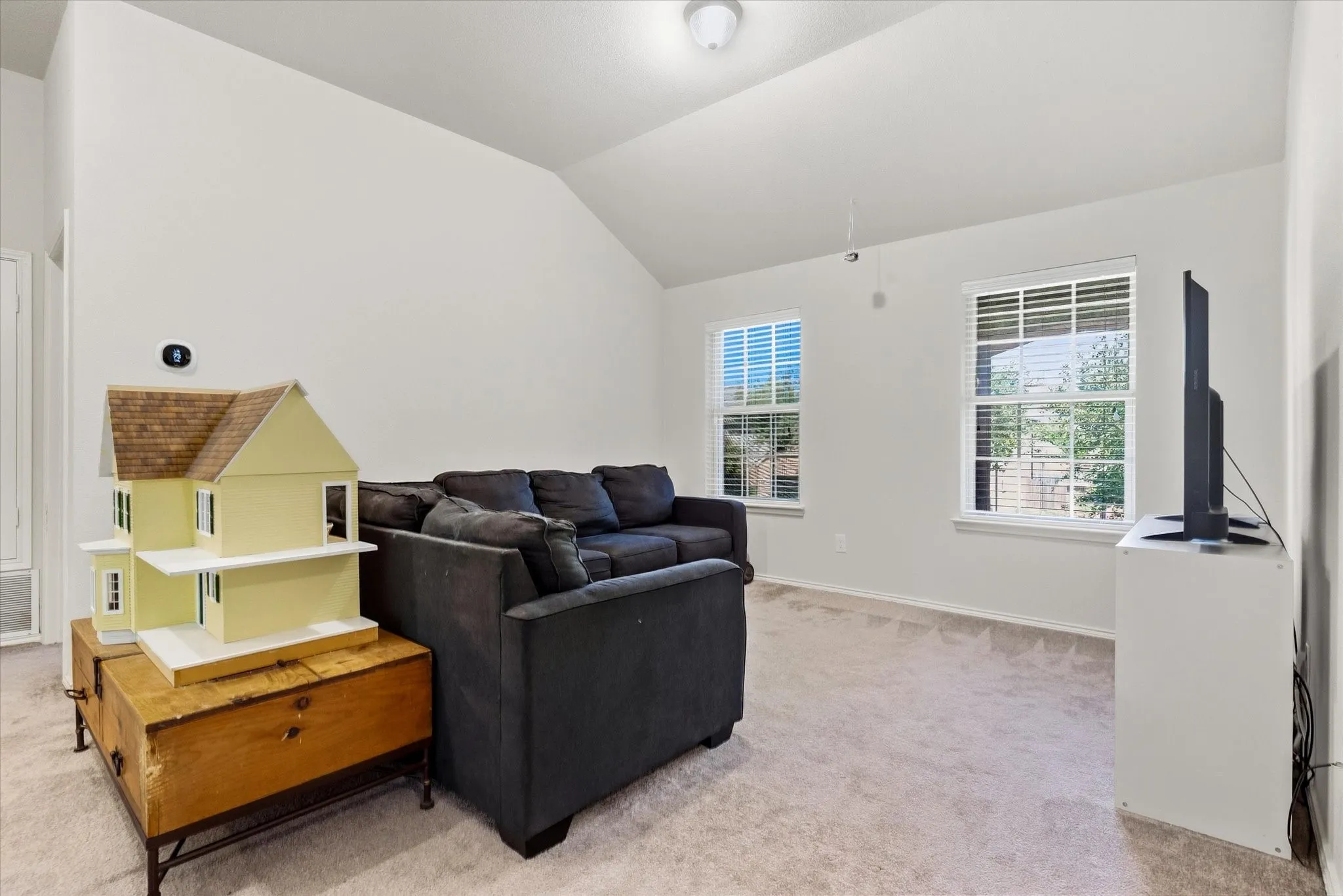 Vaulted ceiling with a flush-mount light fixture, two windows with blinds, and neutral carpeting