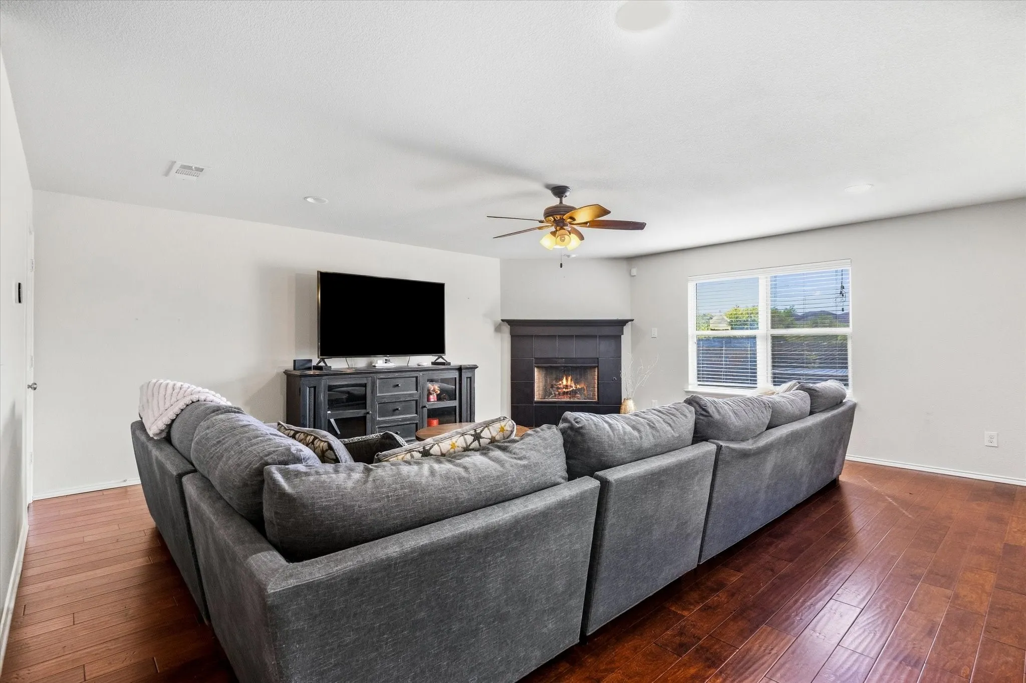 Hardwood-finish flooring, recessed lighting, ceiling fan, corner fireplace with dark mantel, and multiple windows