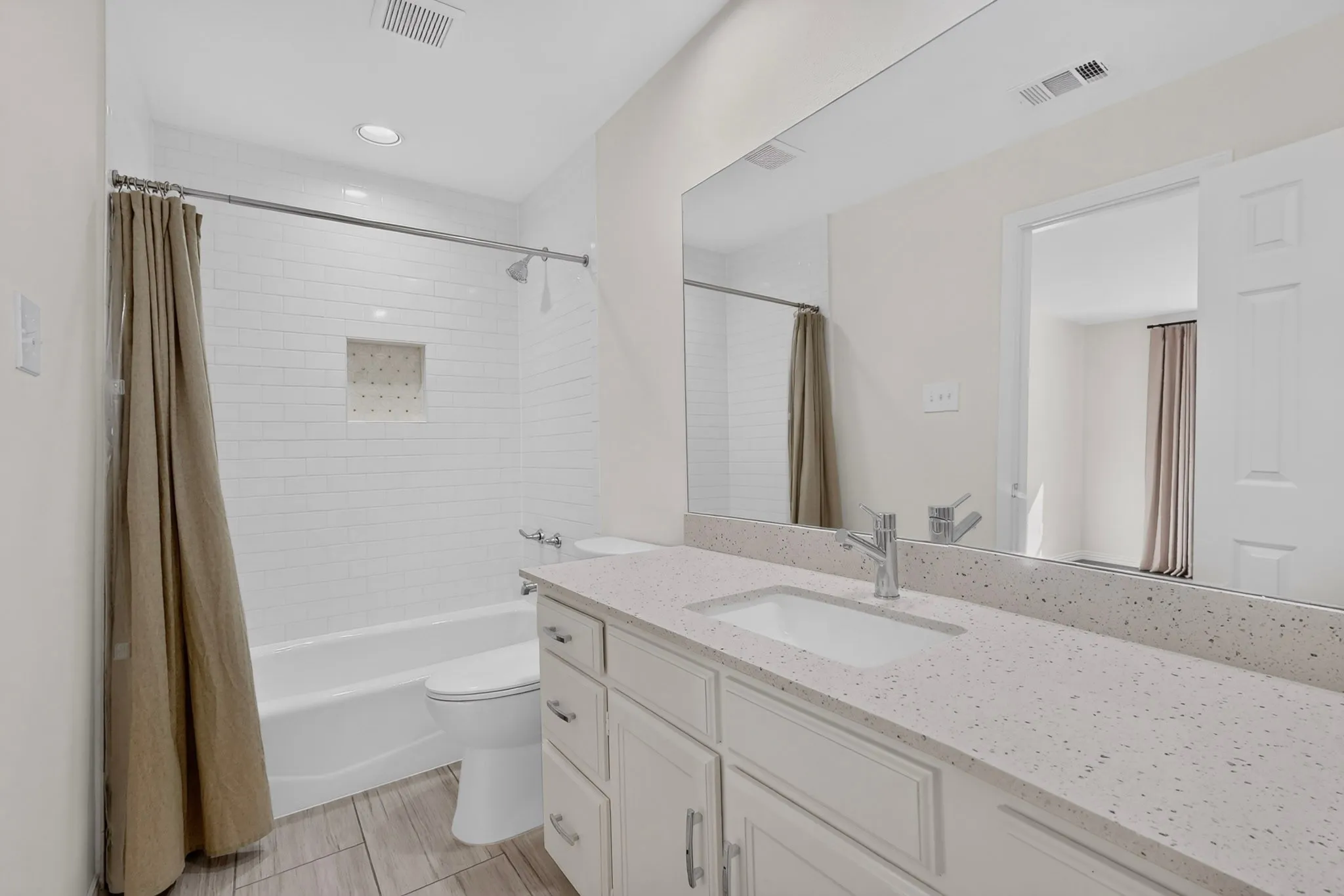 White subway tile shower surround with integrated niche, polished chrome shower fixtures, and a white bathtub
