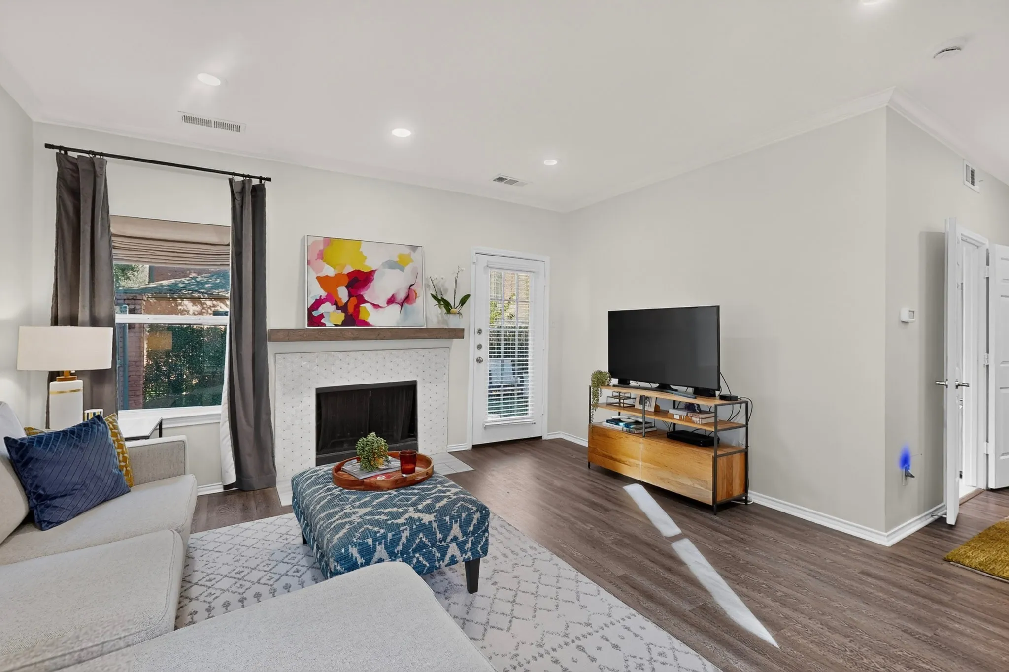 Recessed lighting, crown molding, wood-finish flooring, white brick fireplace with a wood mantle, and a glass-paned door