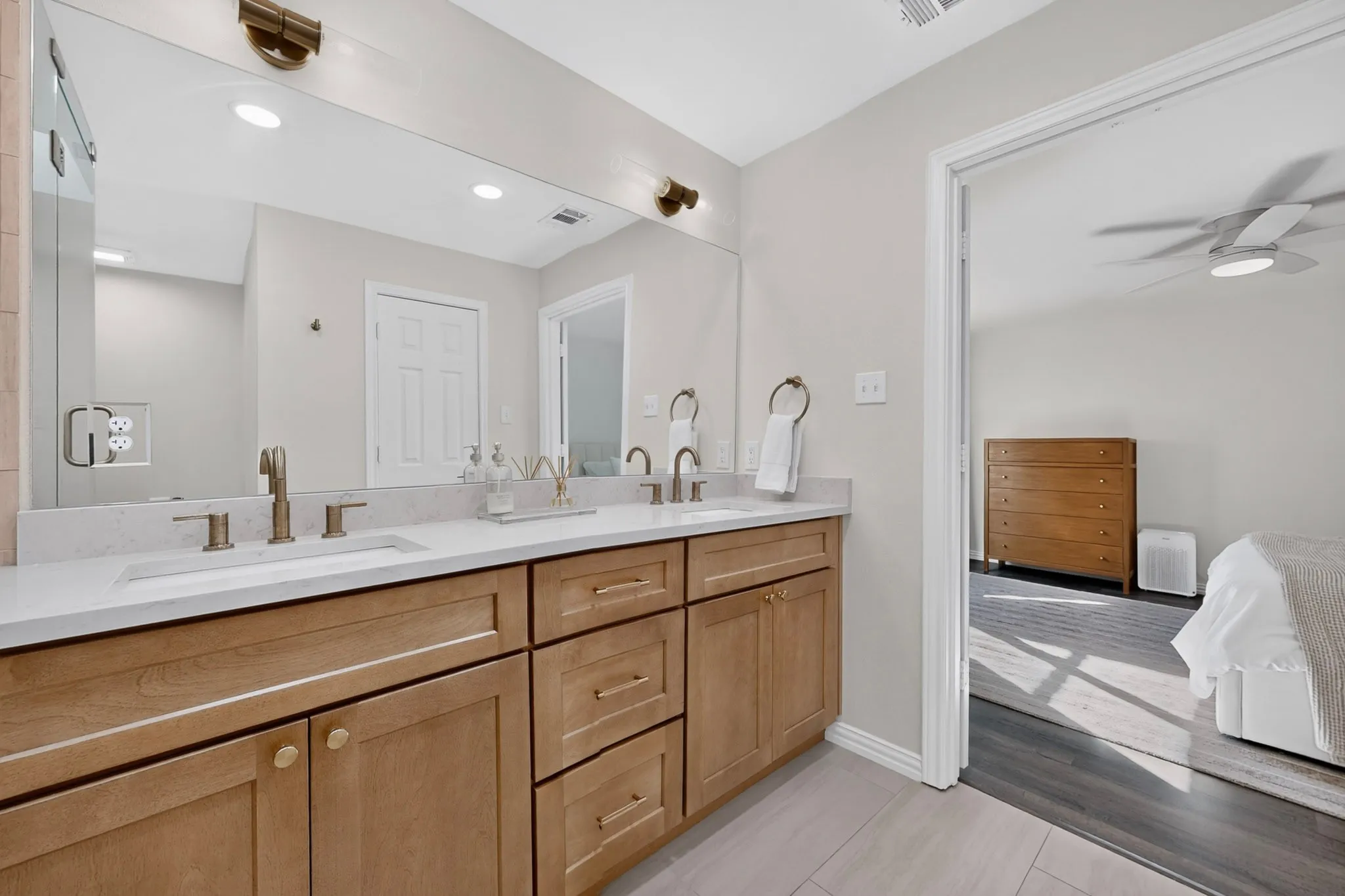 Dual vanity with light wood-finish cabinetry, white countertops, and bronze-finish fixtures