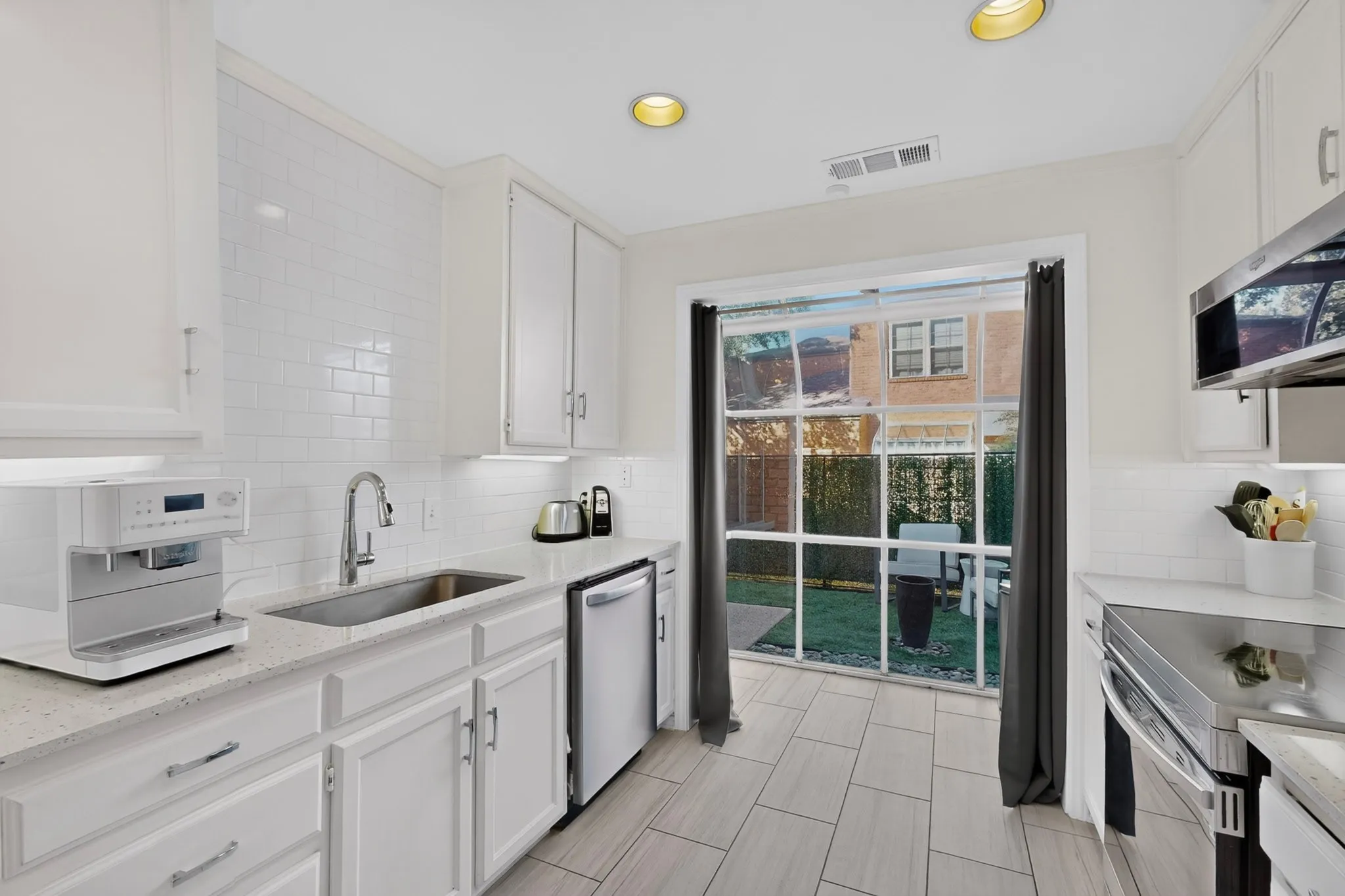 White cabinetry, subway tile backsplash, stainless steel appliances, recessed lighting, and a sliding glass door to an outdoor space