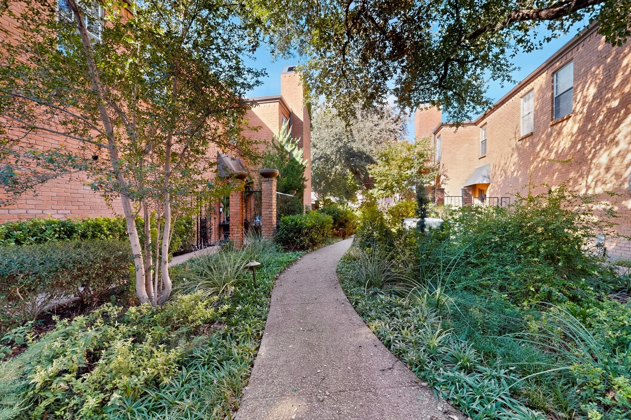 Curved concrete pathway with varied plantings, brick building exteriors, and mature trees