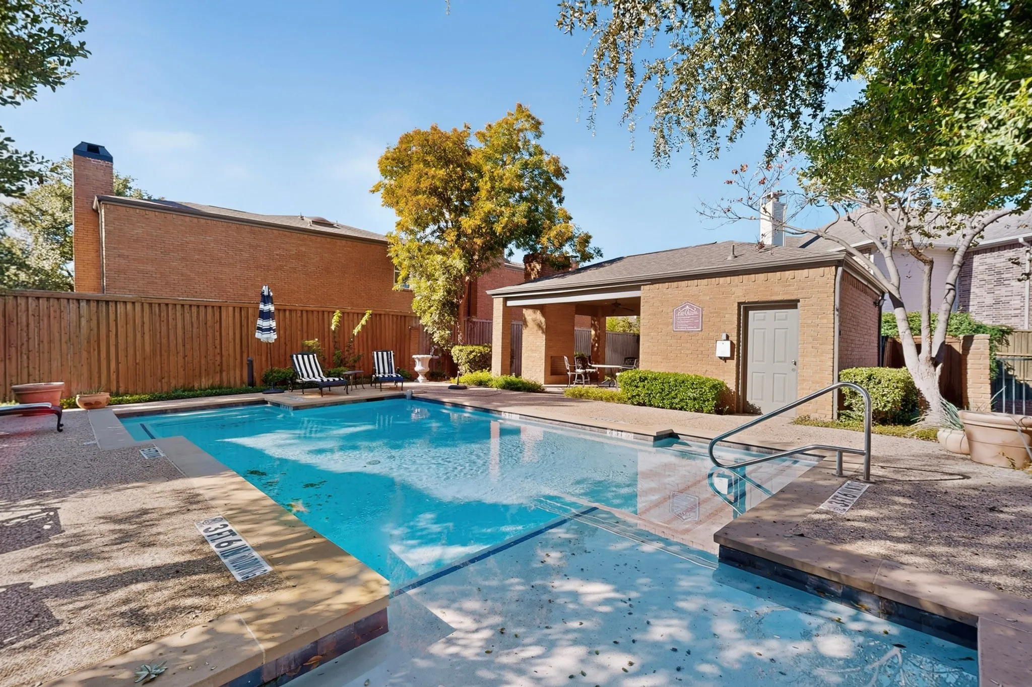 Community Swimming pool with integrated steps, surrounded by a concrete deck and a brick-clad pool house with an open-air covered patio