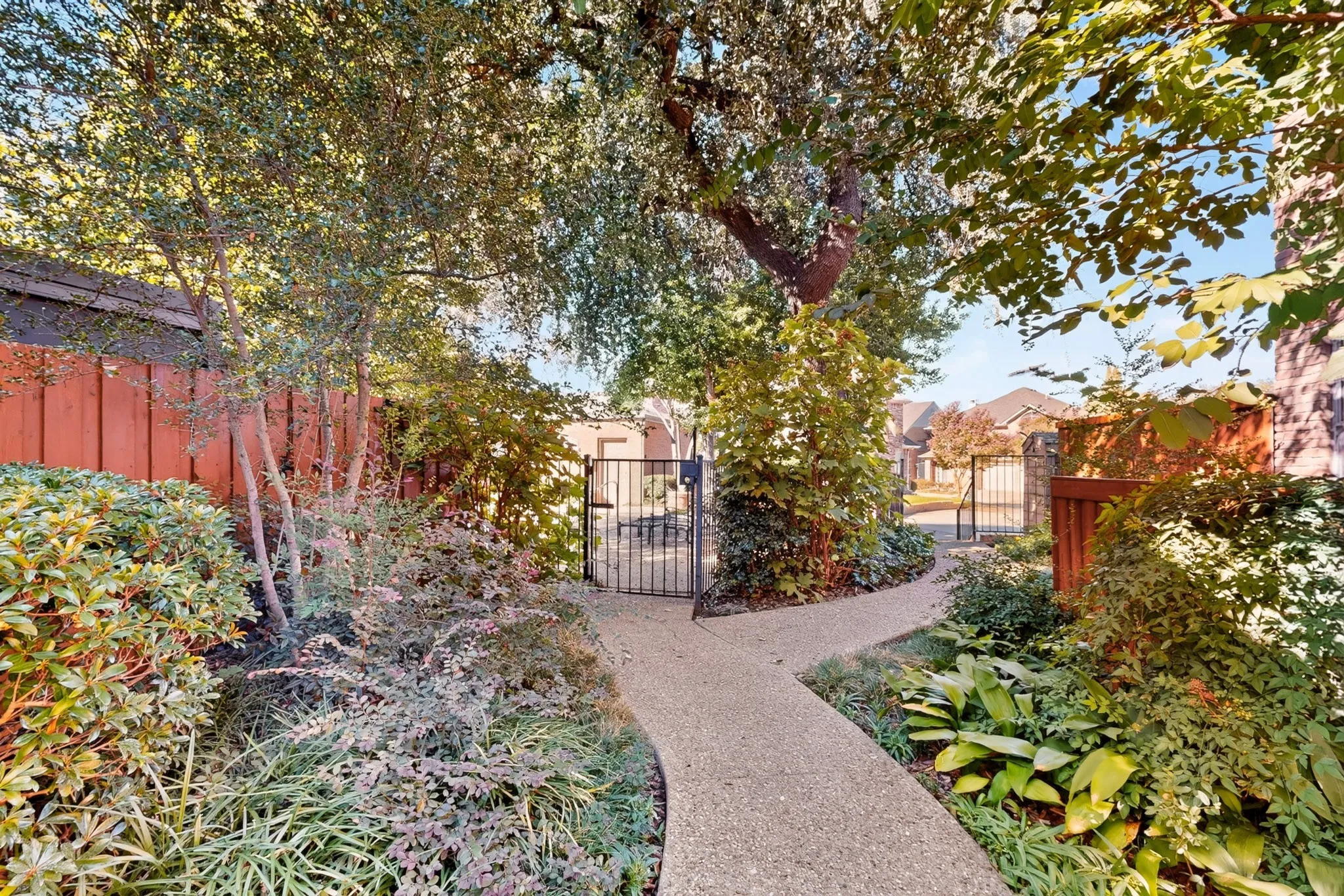 Paved walkway with lush landscaping, mature trees, and a decorative metal gate