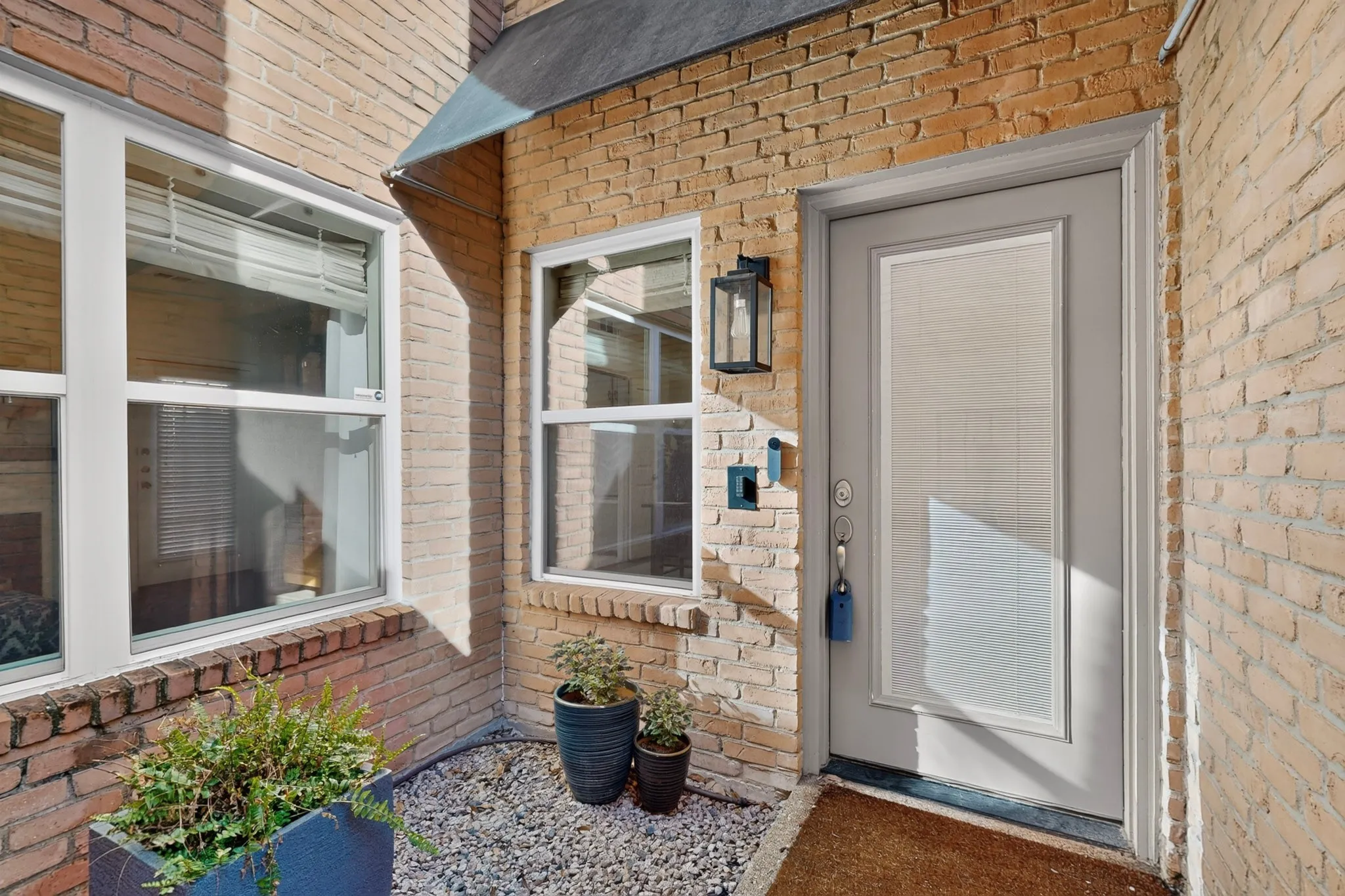 Brick exterior featuring white-framed windows, an entryway door with an opaque glass insert, and a black exterior wall lantern