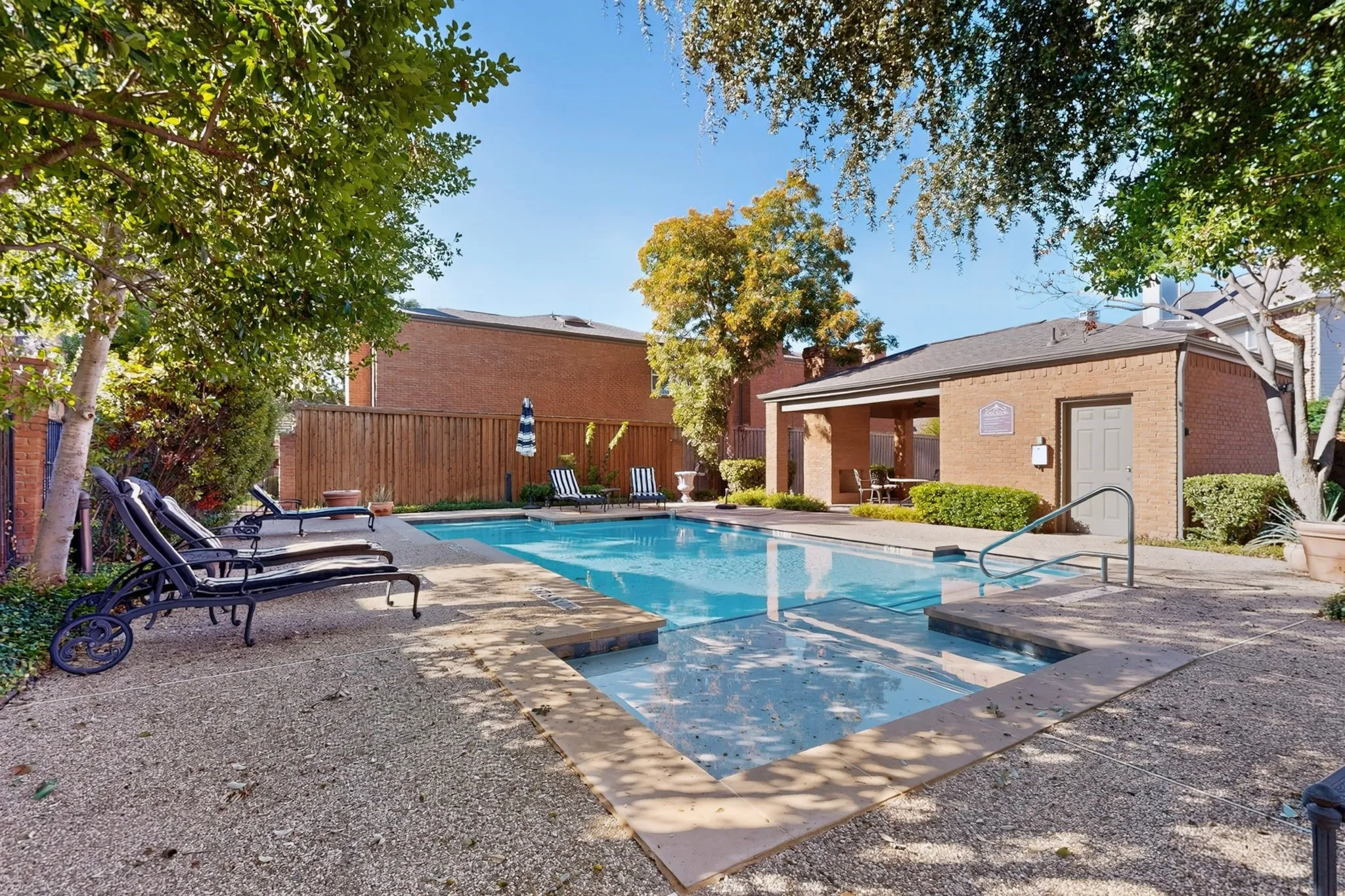 Community Swimming pool with concrete decking, surrounding gravel, and mature landscaping