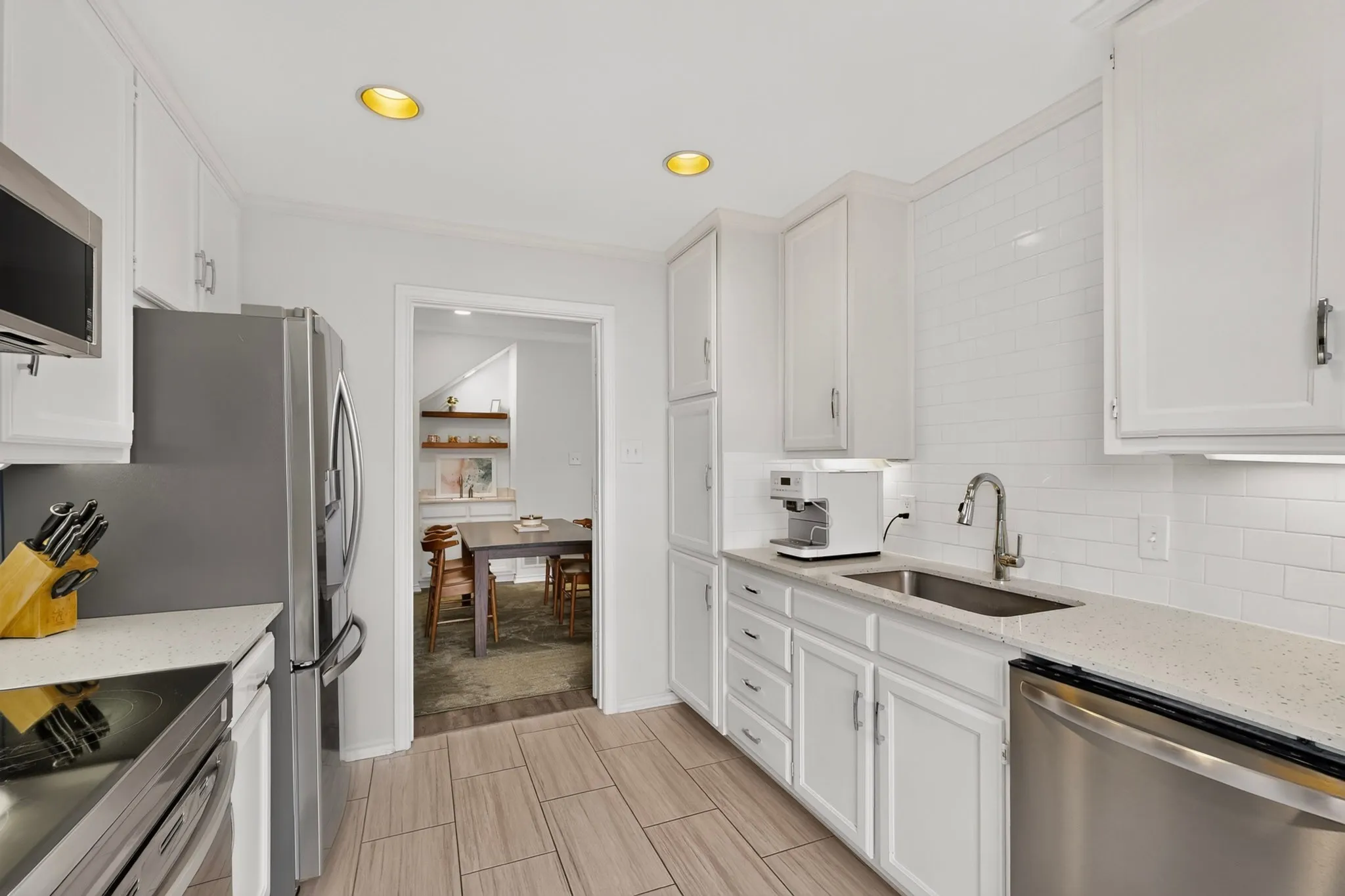 White cabinetry with crown molding, stainless steel appliances, light-toned countertops, white subway tile backsplash, and wood-finish flooring