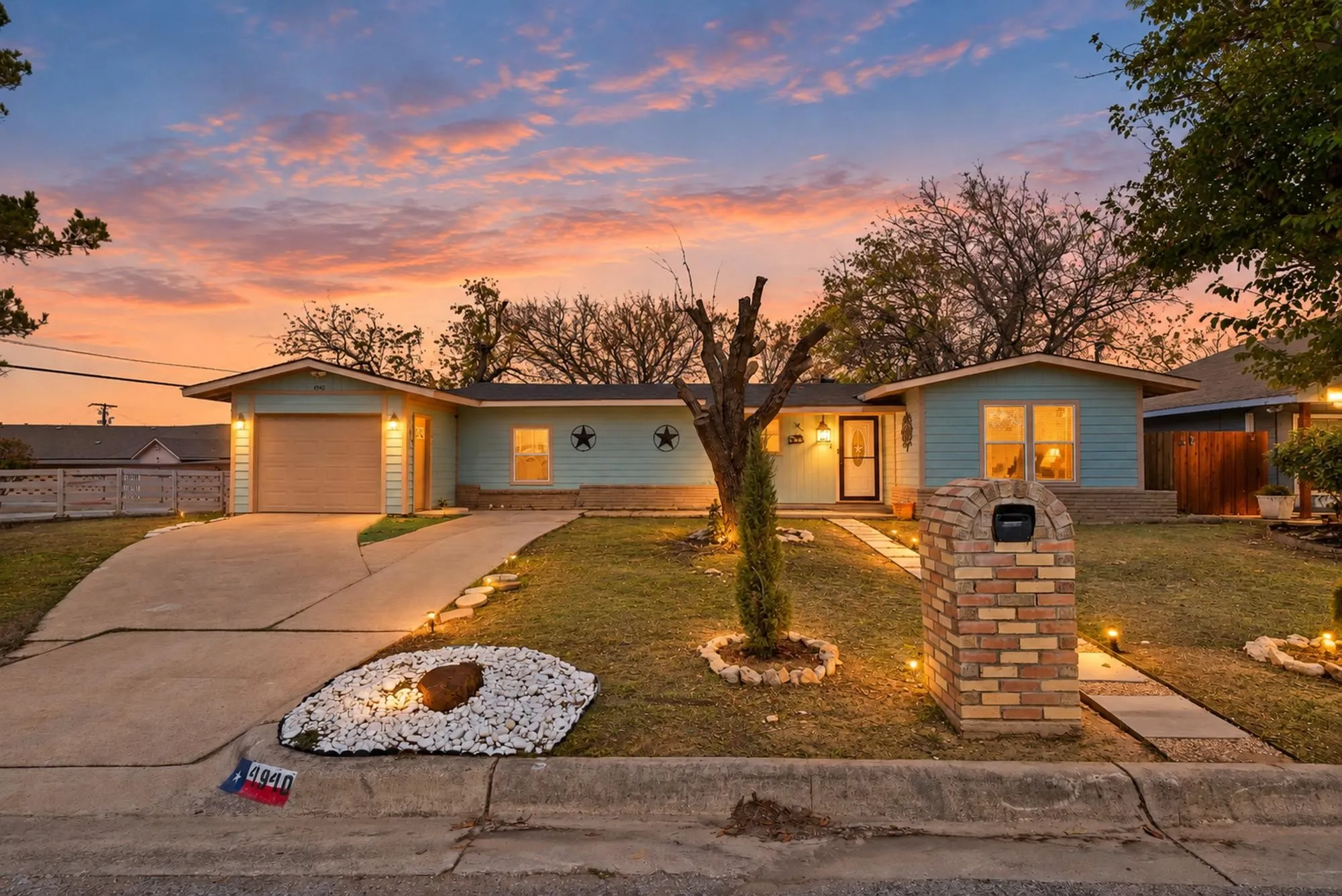 Light blue horizontal siding, front-facing garage with a wood-finish door, brick mailbox with an arched top, concrete driveway, and a stone paver walkway