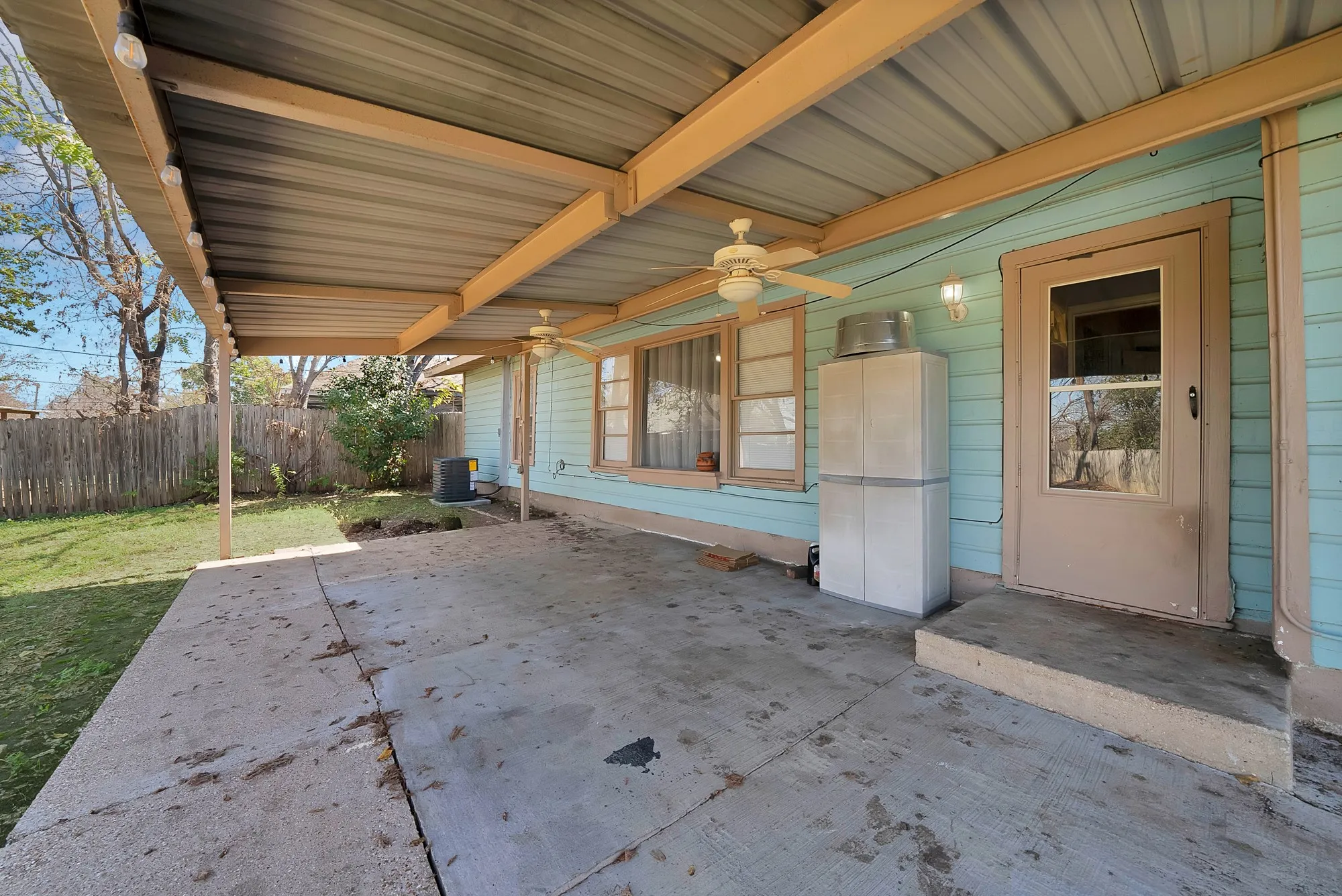 Covered concrete patio with ceiling fans and wood fence
