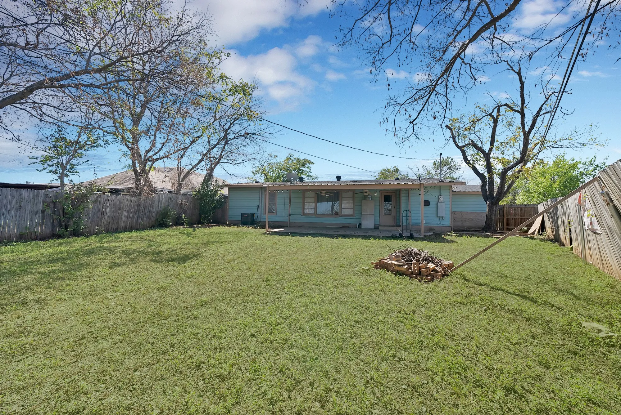 Expansive rear yard with a grass lawn, mature trees, and wood fencing