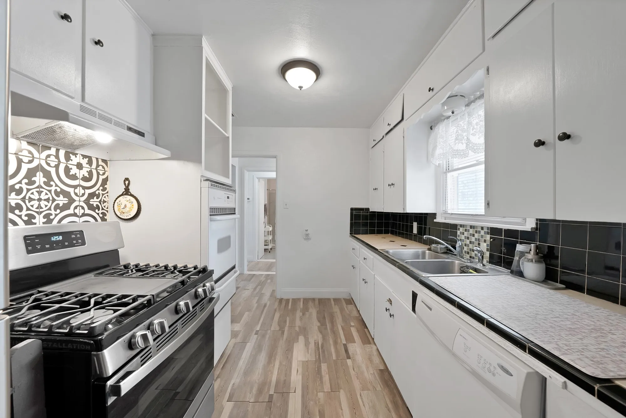 Galley kitchen with wood-finish flooring, white cabinetry, and stainless steel range