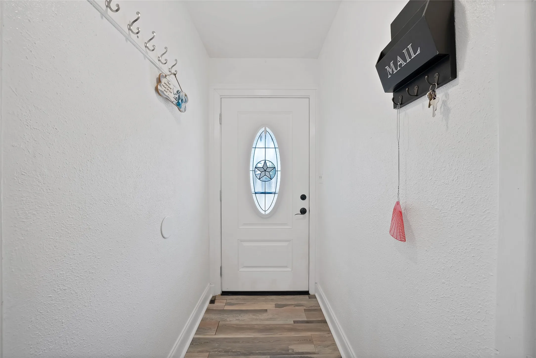 Welcoming entryway featuring a classic white six-panel entry door with decorative glass insert, wood-finish flooring, and clean white walls