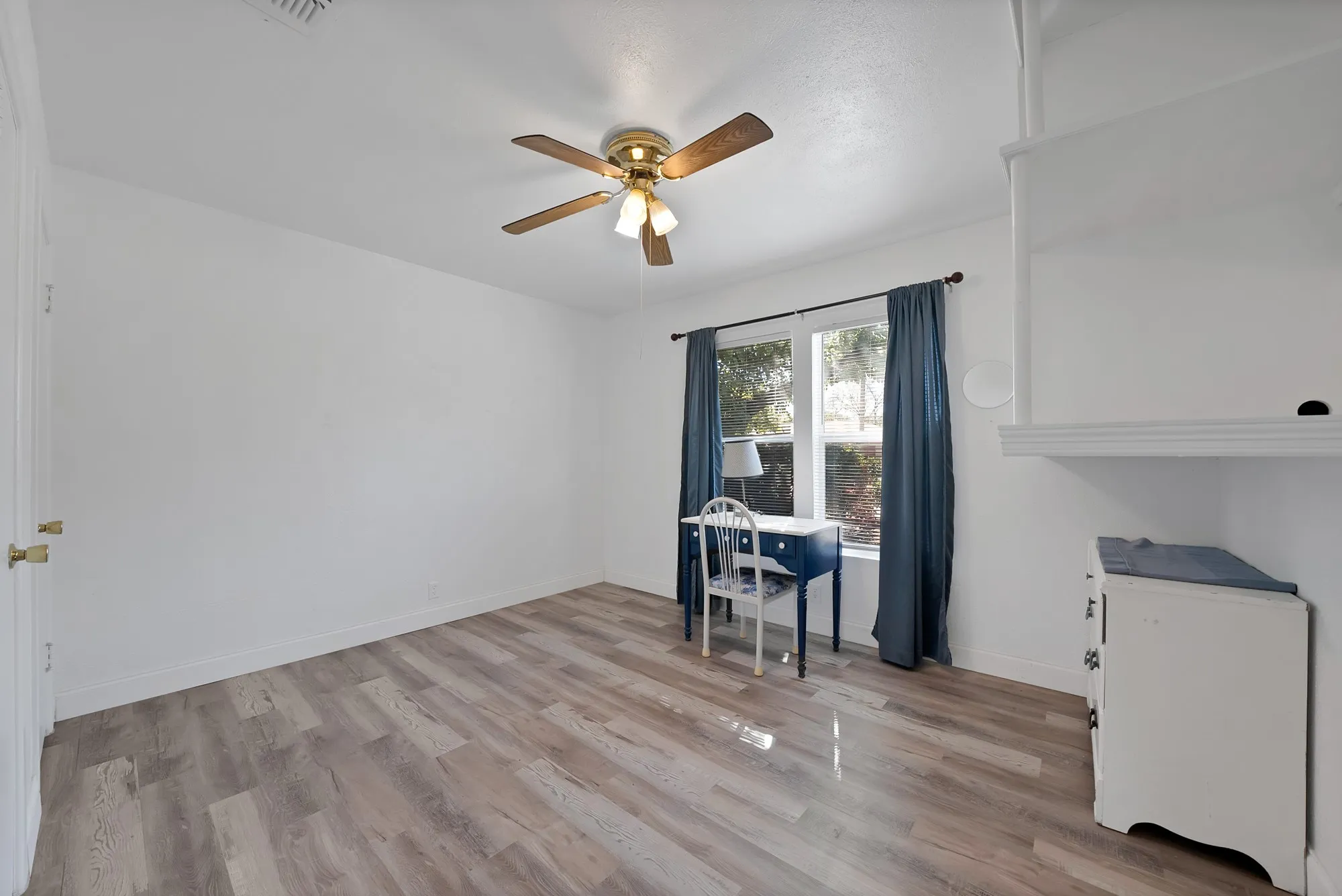 Recessed window with dark drapes, wood-finish flooring, ceiling fan with light fixture, and built-in shelving