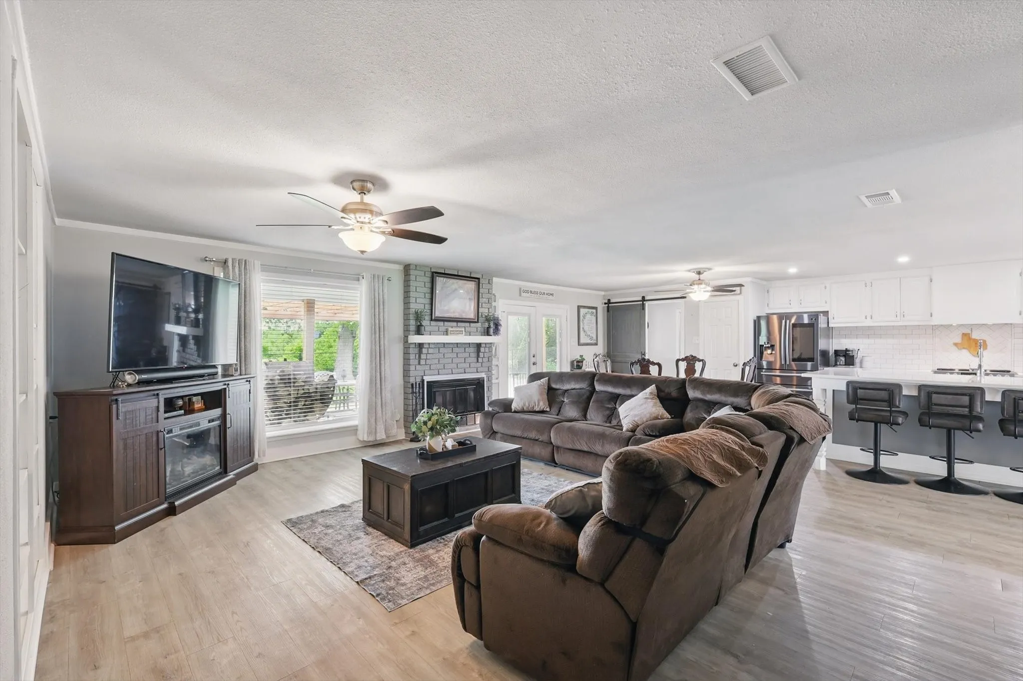 Open-concept living space featuring wood-finish flooring, a brick-surround fireplace, and a ceiling fan