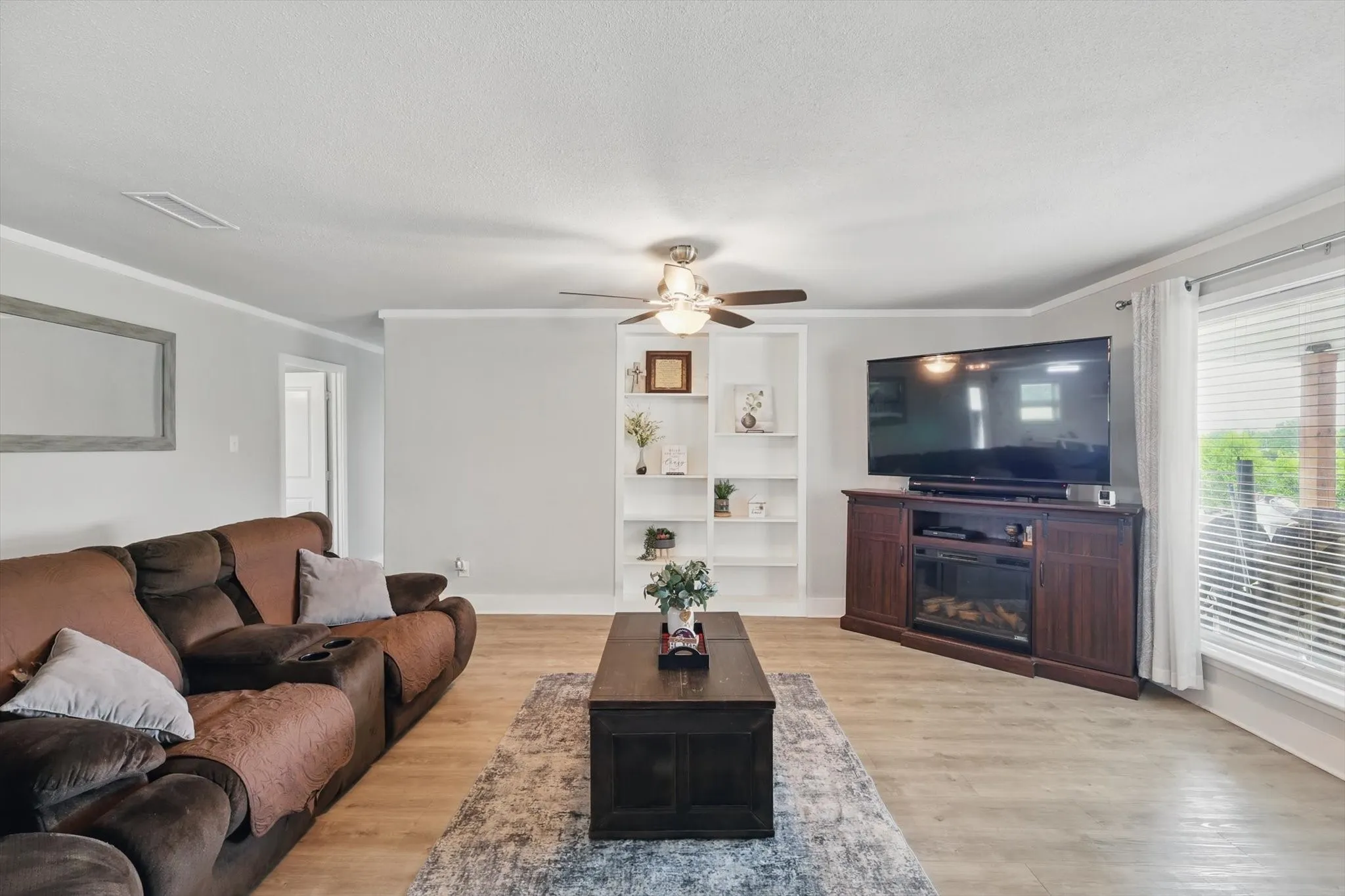 Recessed built-in shelving, ceiling fan with integrated lighting, wood-finish flooring, and crown molding