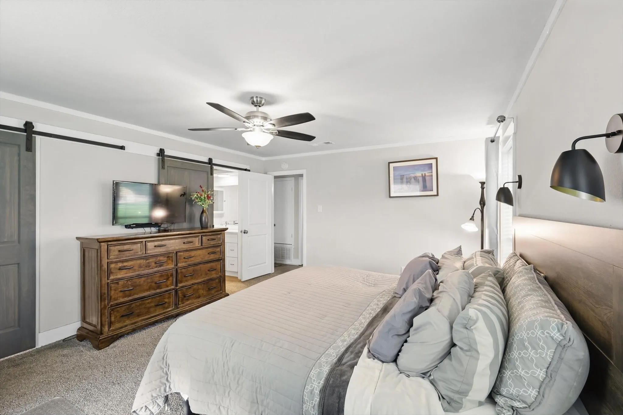 Ceiling fan with integrated lighting, two barn doors with dark wood finish, wall-mounted sconce lighting, and crown molding