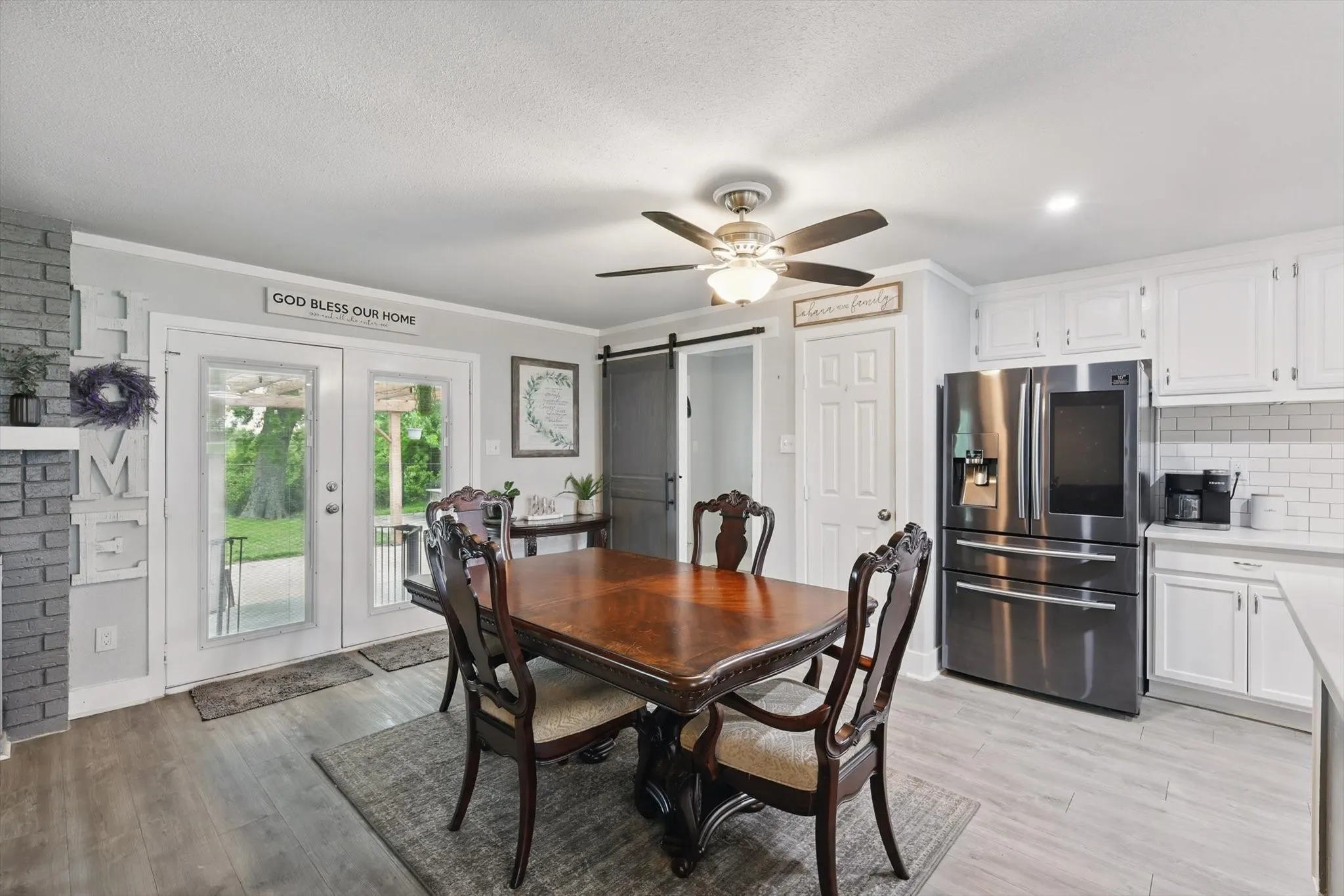 Open kitchen and dining area featuring stainless steel appliances, white cabinetry, subway tile backsplash, wood-finish flooring, and a ceiling fan with integrated lighting