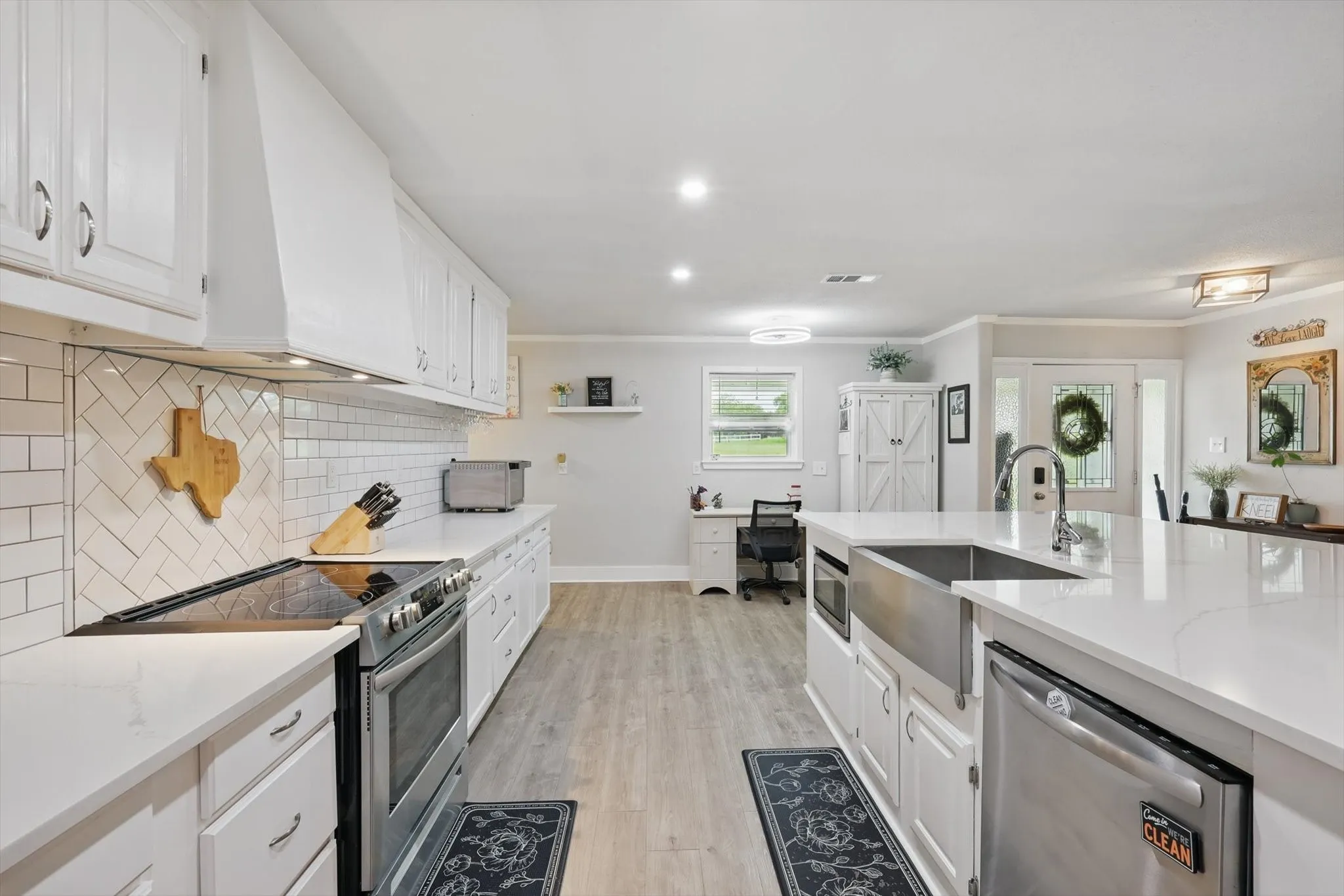 Spacious kitchen featuring white cabinetry, light-toned countertops, a stainless steel farm sink, and wood-finish flooring
