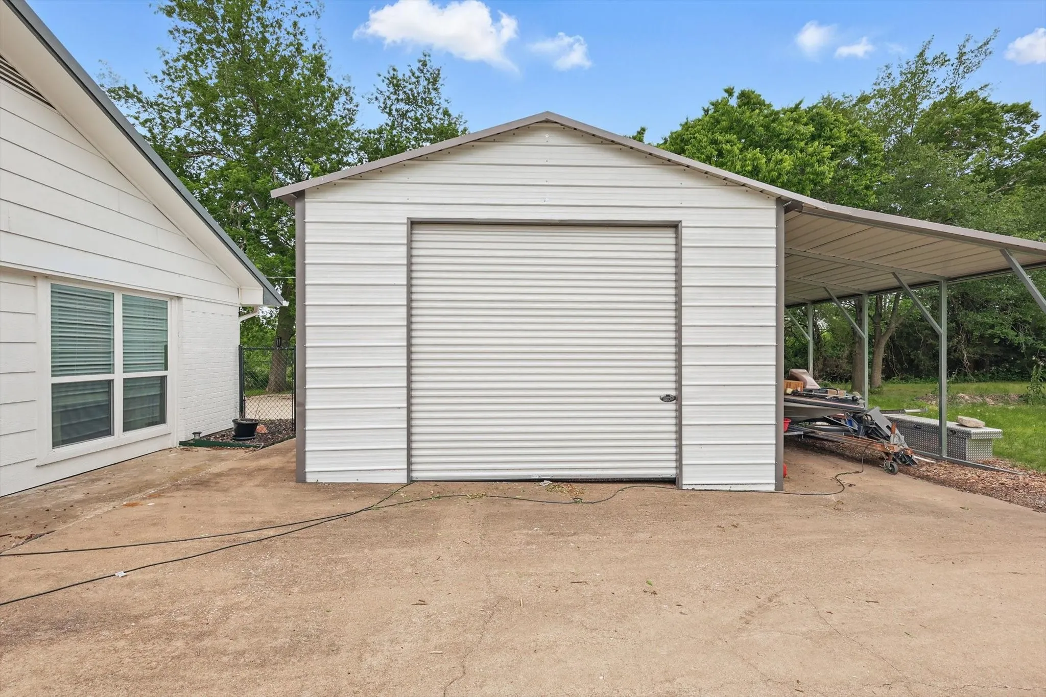 Metal utility building with a roll-up door, an attached open-sided carport, and a concrete pad
