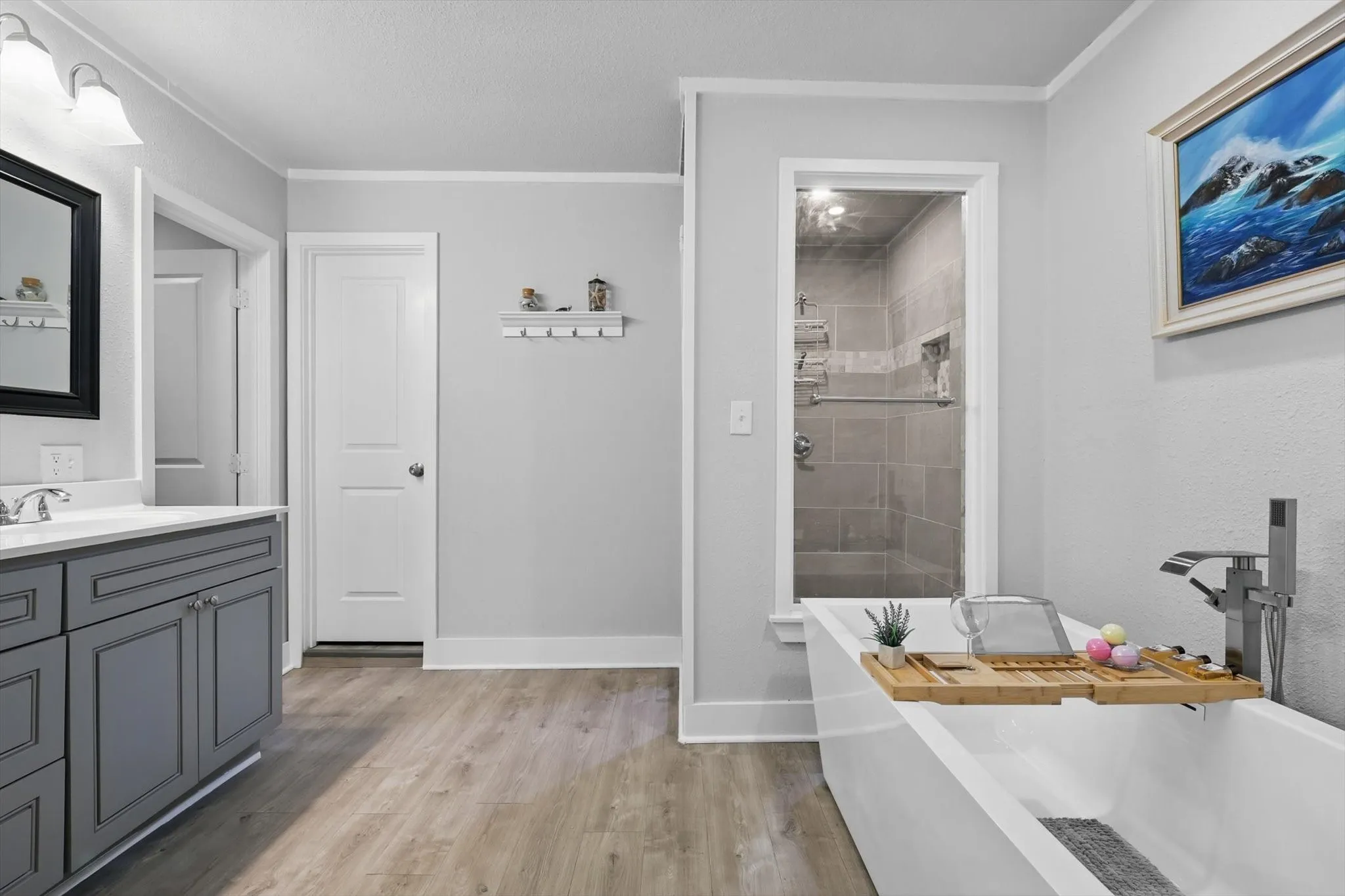 Spa-inspired primary bathroom featuring a freestanding soaking tub with chrome fixtures, wood-finish flooring, and a walk-in shower with tile surround