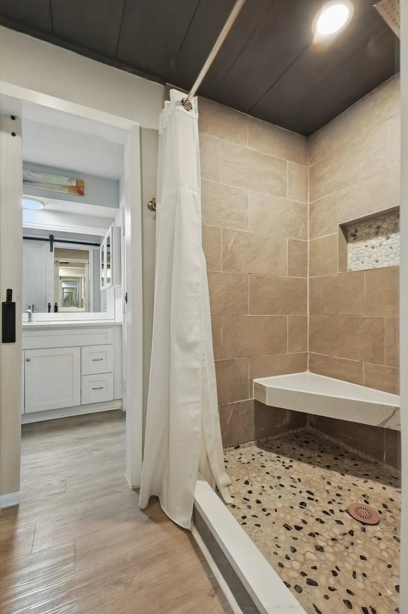 Tiled shower with a corner bench, pebble flooring, and built-in niche