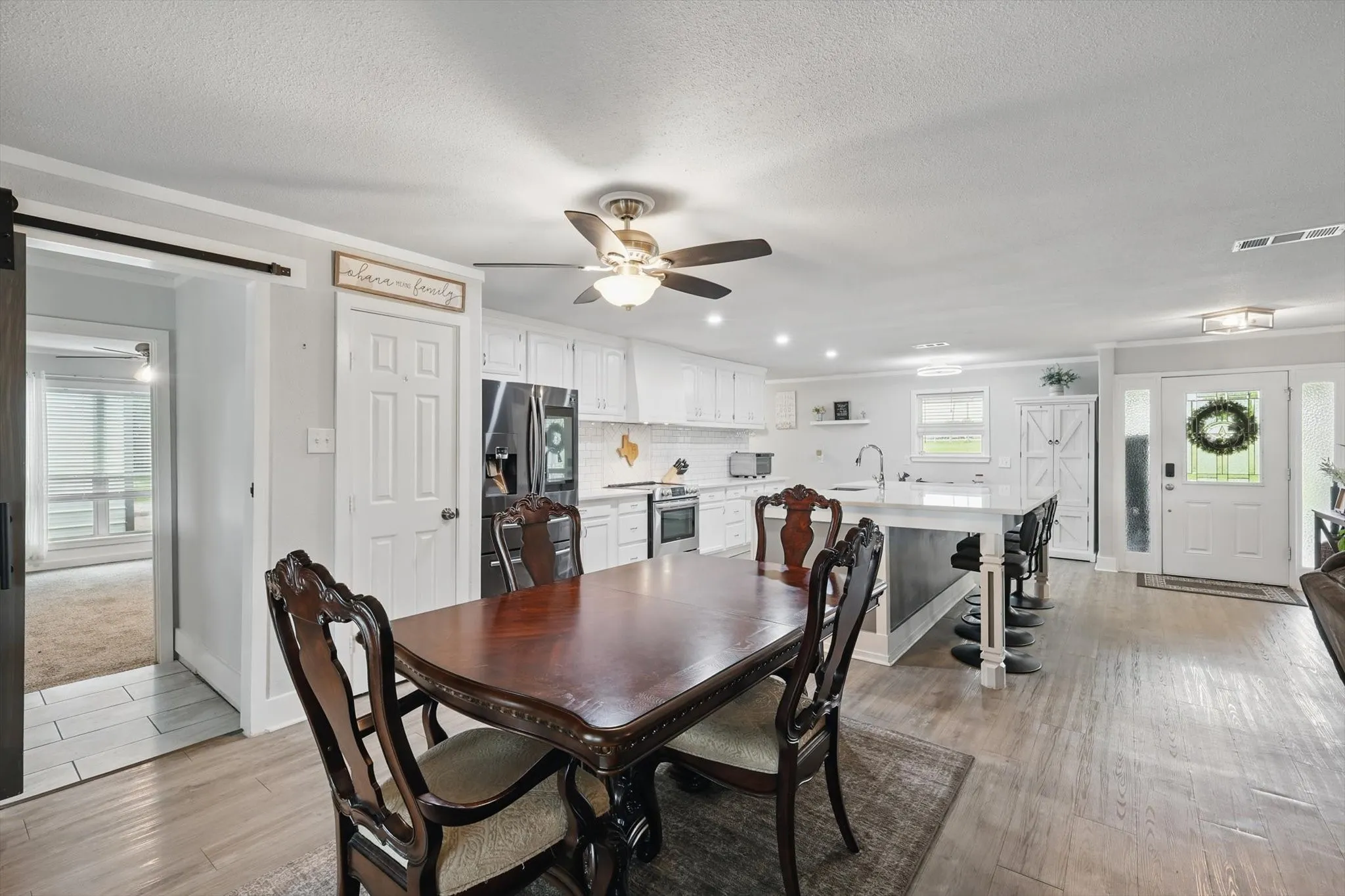 Open-concept living space featuring wood-finish flooring, white kitchen cabinetry, a kitchen island with seating, a ceiling fan, and a barn door entry
