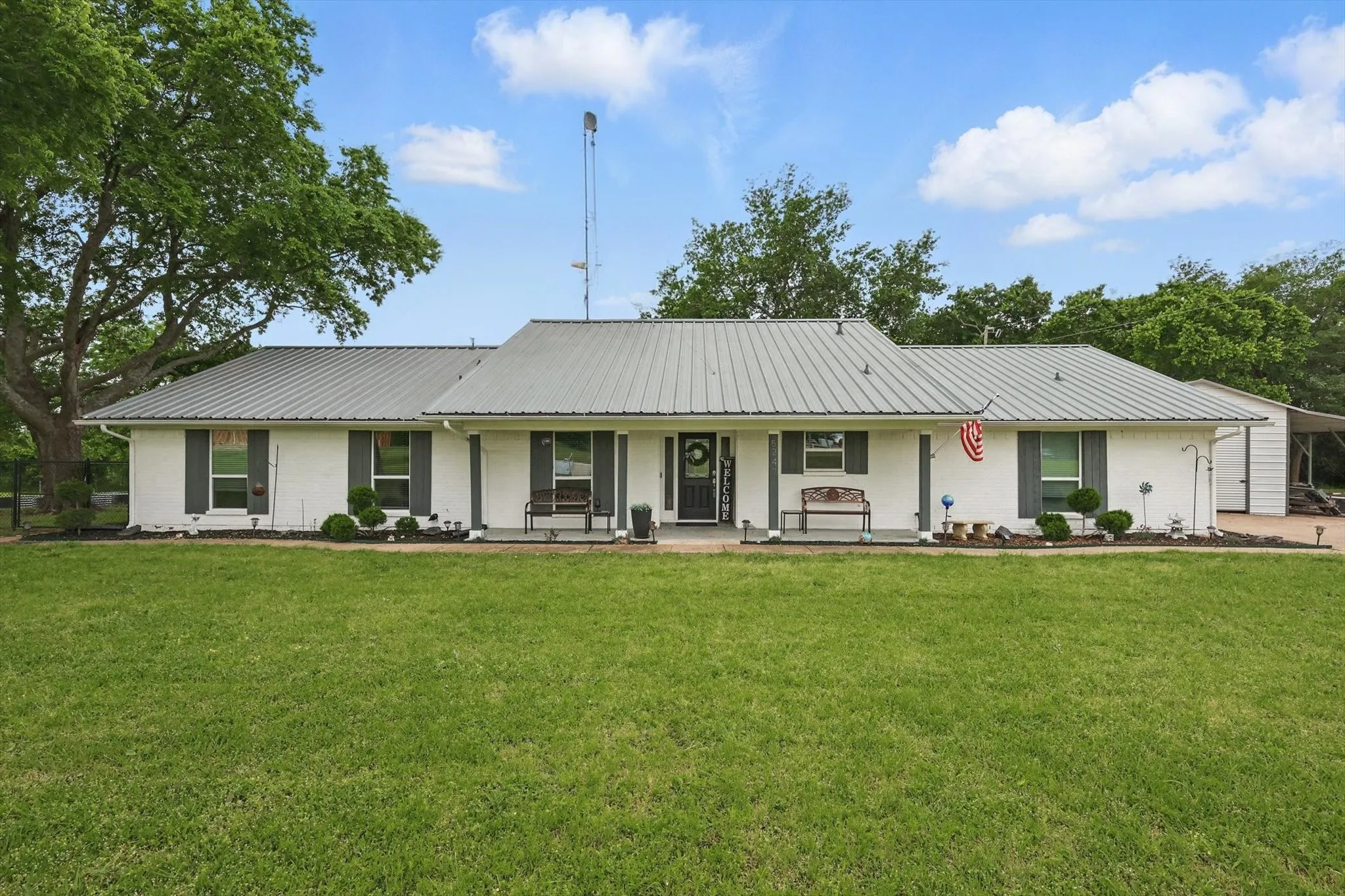 White brick exterior with a metal roof, covered front porch, and established landscaping