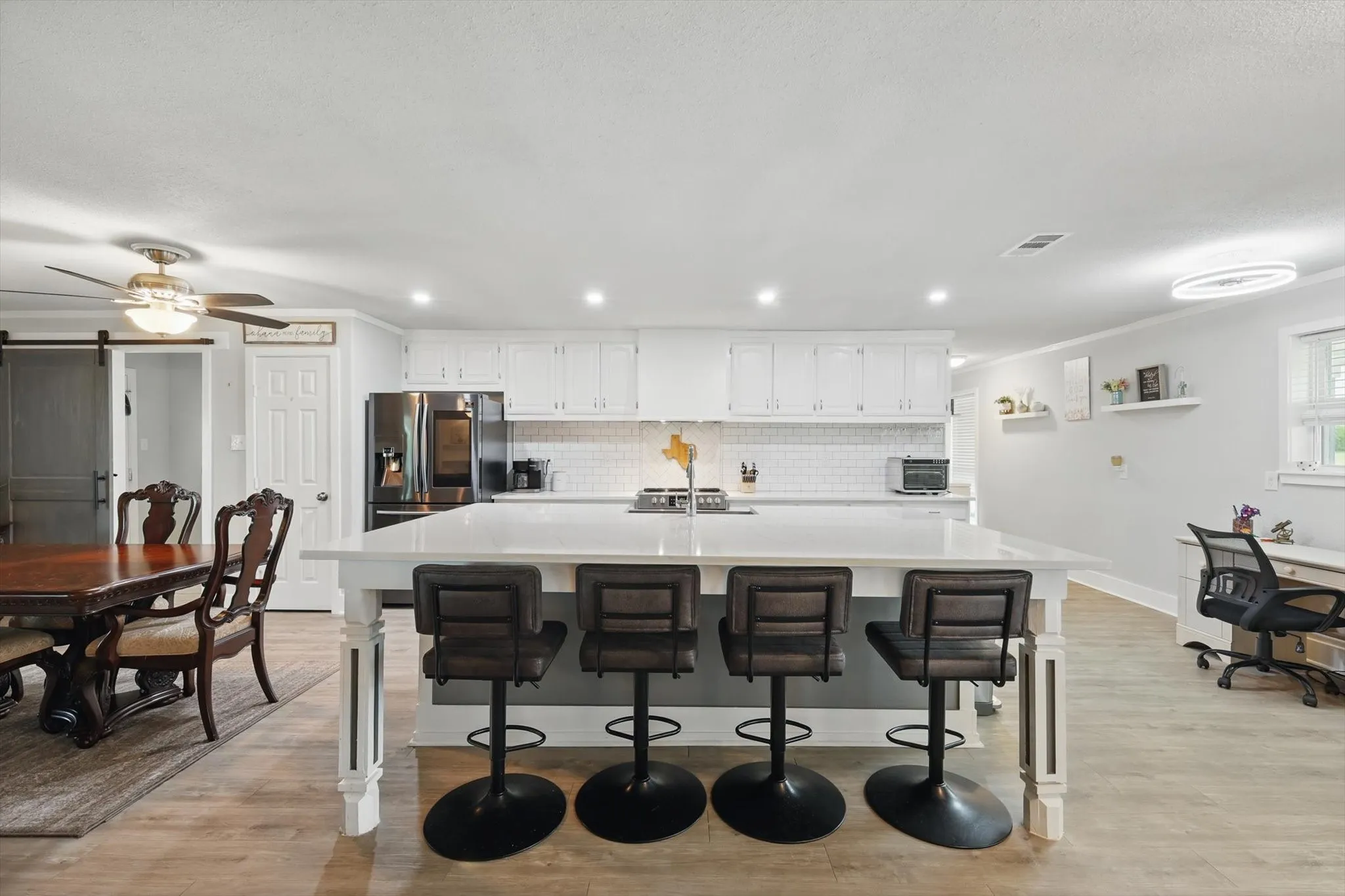 Open-concept kitchen and dining area featuring white cabinetry, stainless steel appliances, quartz countertops, a large waterfall-edge island with seating for four, and wood-finish flooring throughout the space