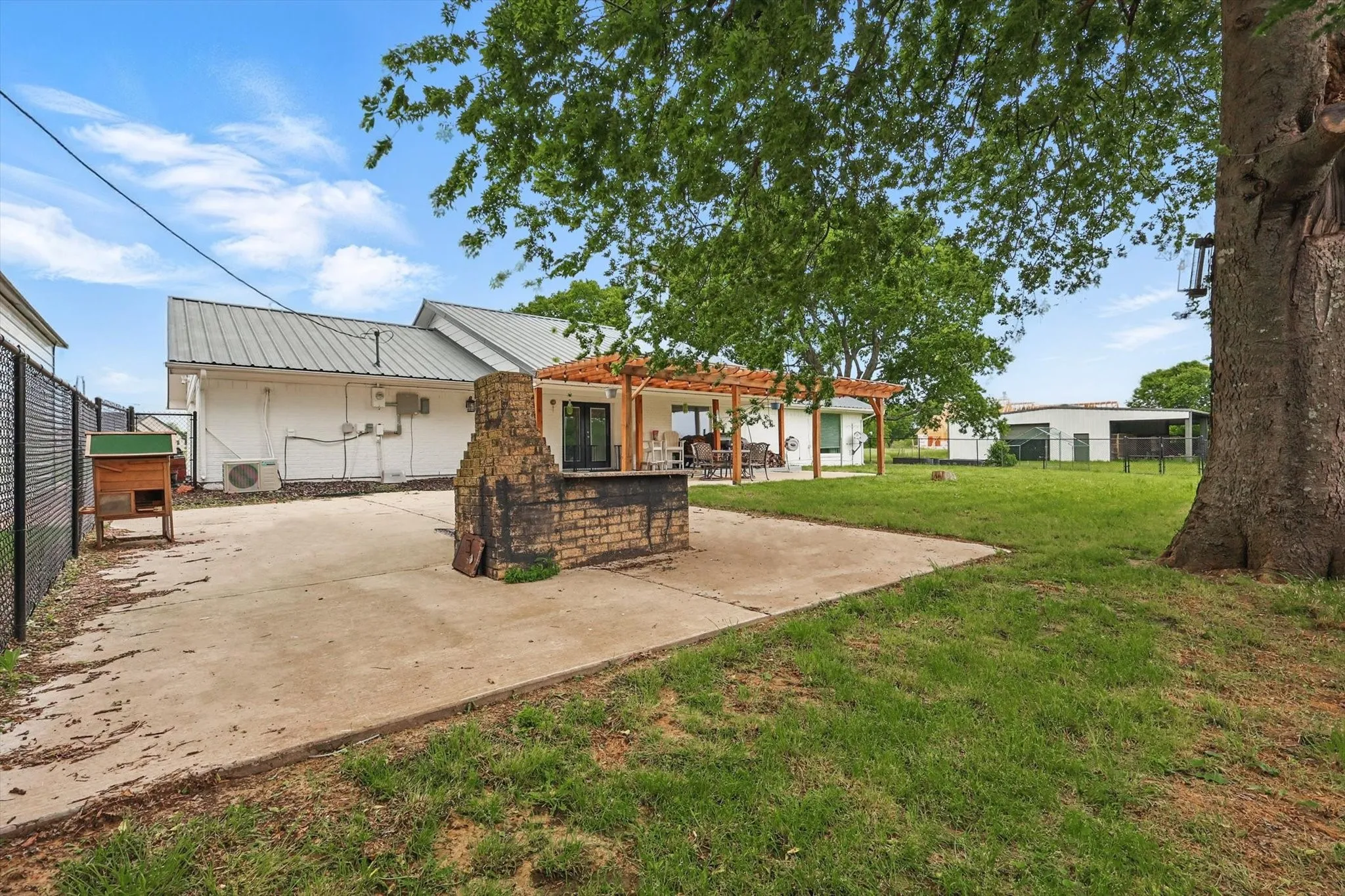 Concrete patio with a built-in brick grilling station, a pergola, and a grassy yard area