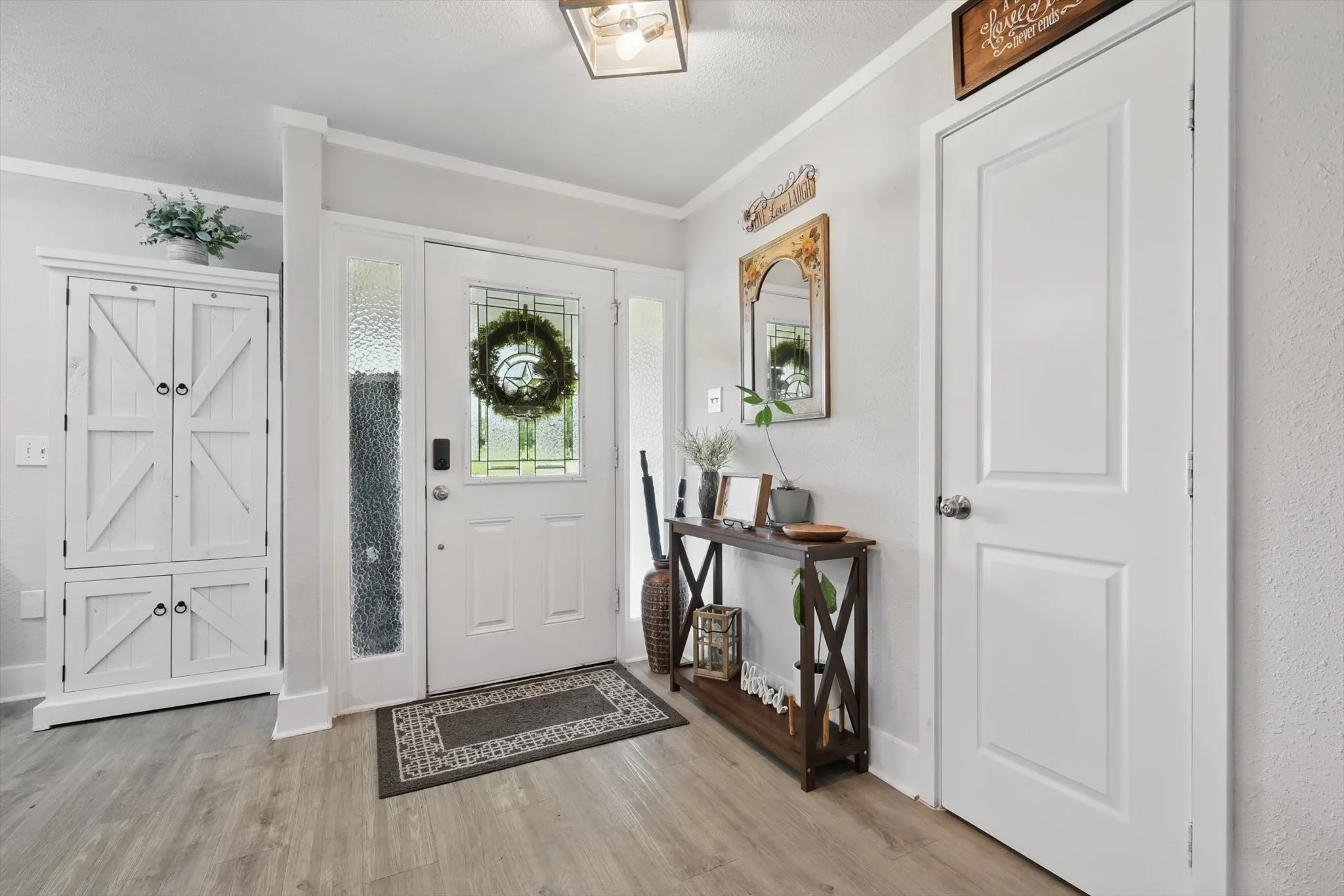 Welcoming foyer showcasing white six-panel doors, wood-finish flooring, geometric entry mat, and decorative wall-mounted mirrors