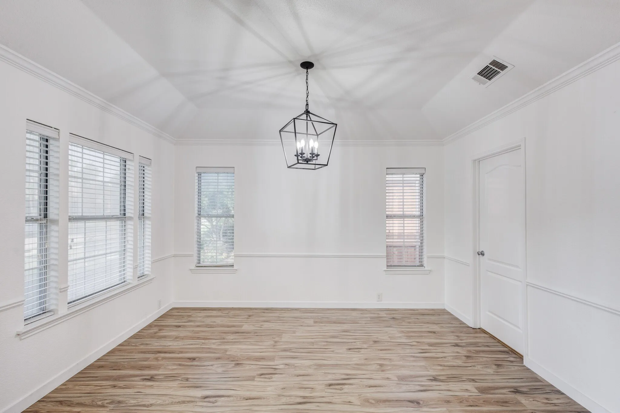 Spare room featuring an inviting chandelier, ornamental molding, lofted ceiling, and light hardwood / wood-style floors