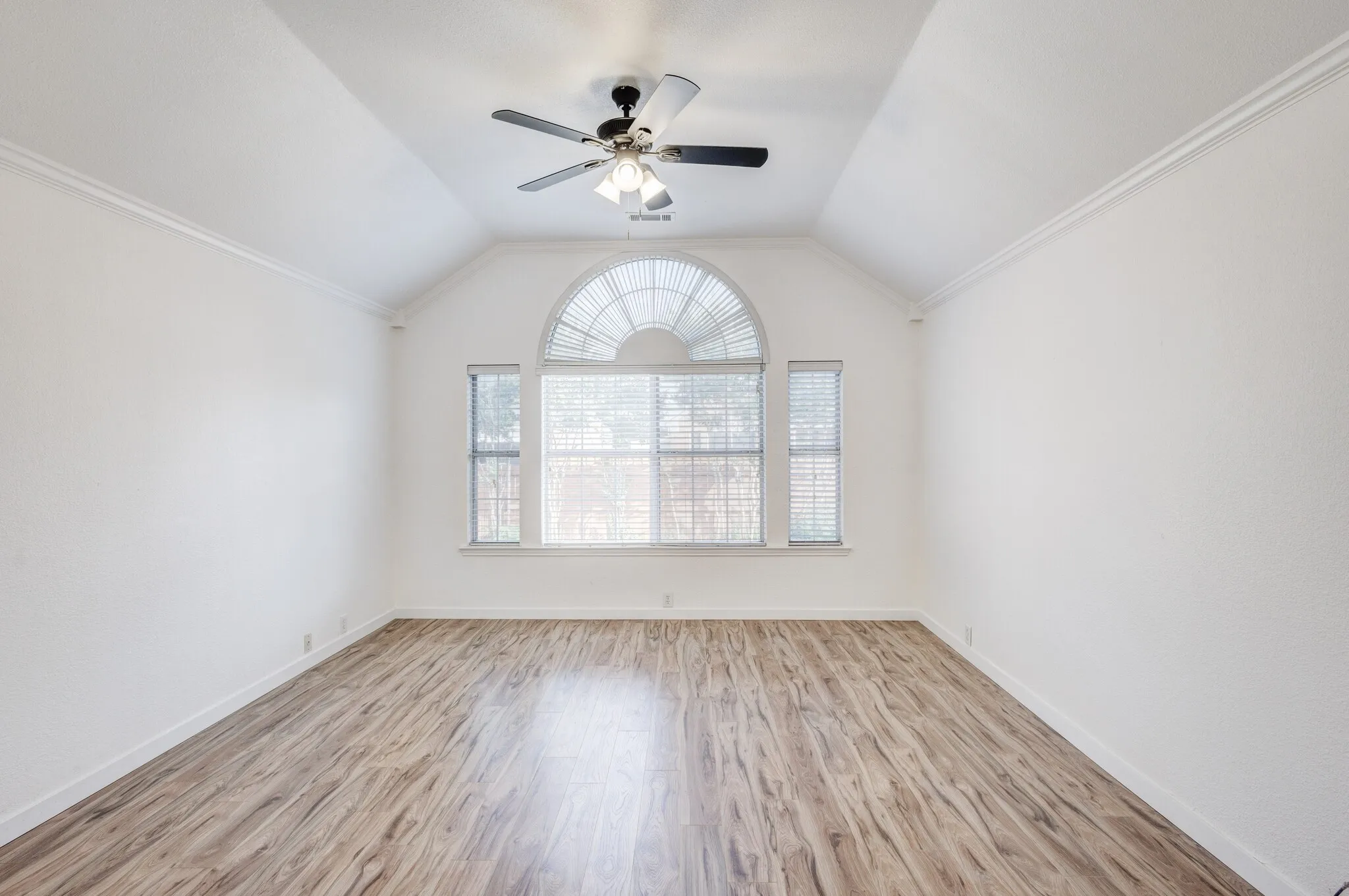Empty room with light hardwood / wood-style floors, ornamental molding, ceiling fan, and vaulted ceiling