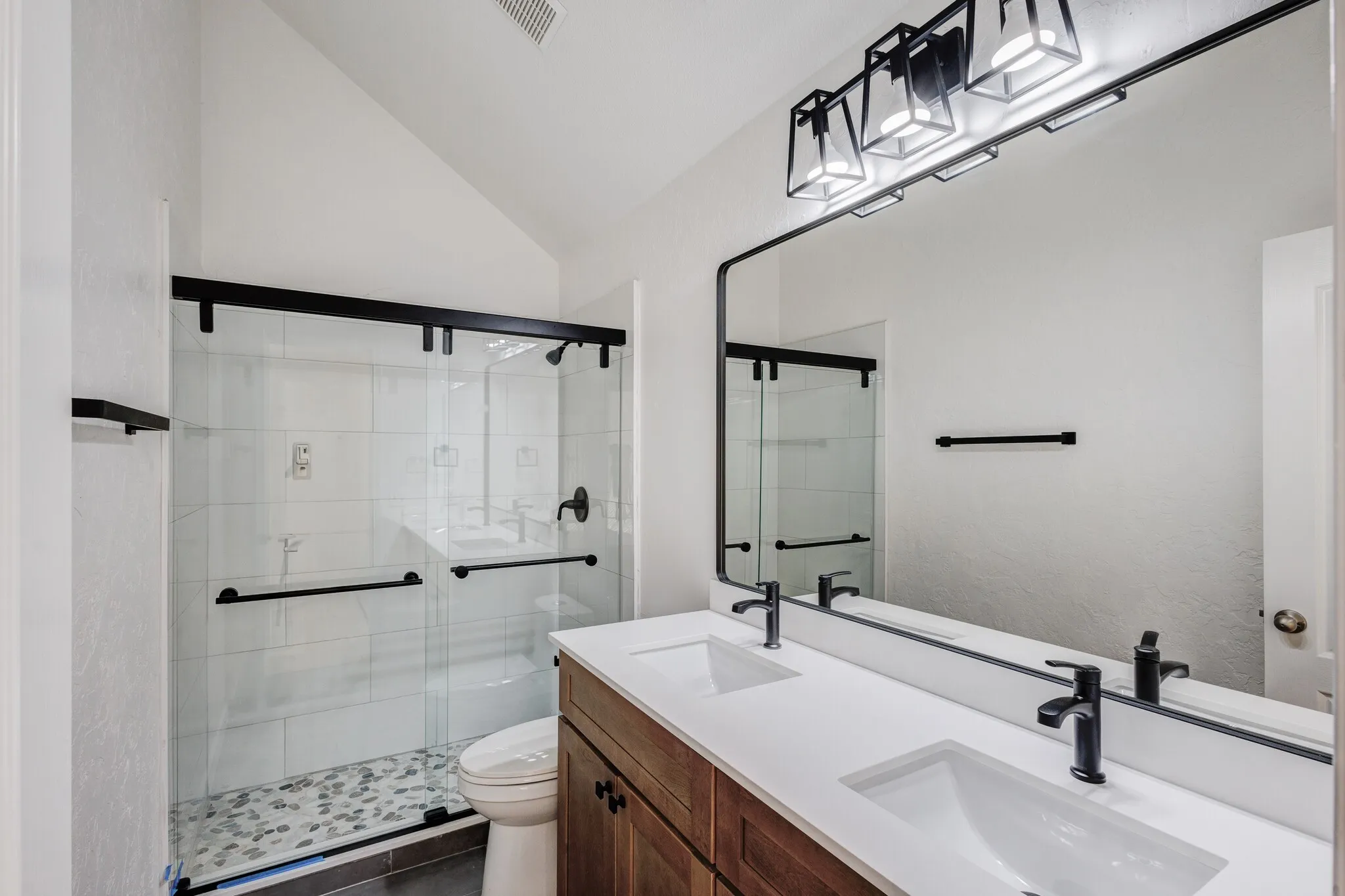 Bathroom with a shower with door, vaulted ceiling, double vanity, tile patterned floors, and toilet