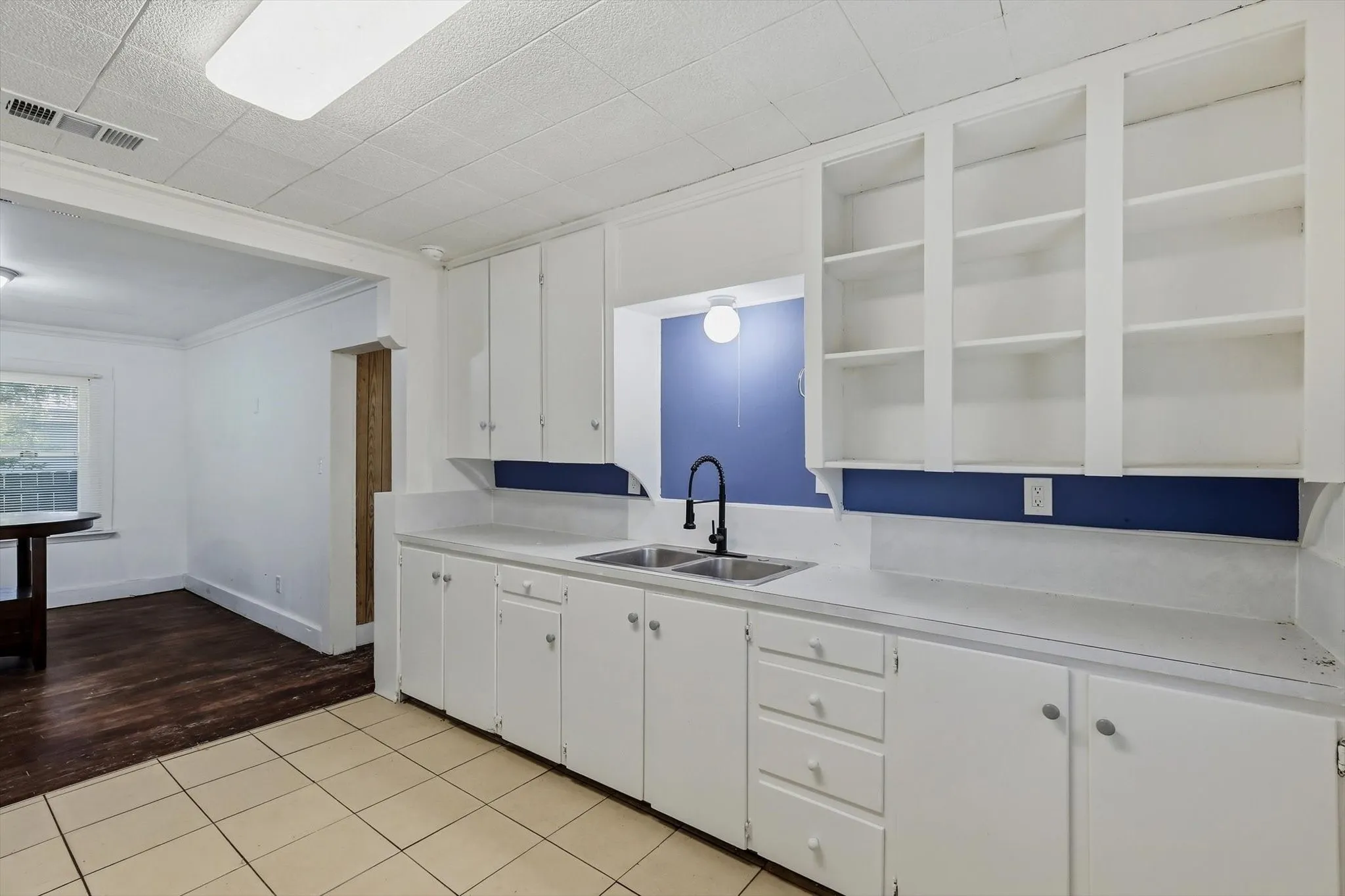 White cabinetry with open shelving, dual basin sink with a matte black faucet, and tiled flooring
