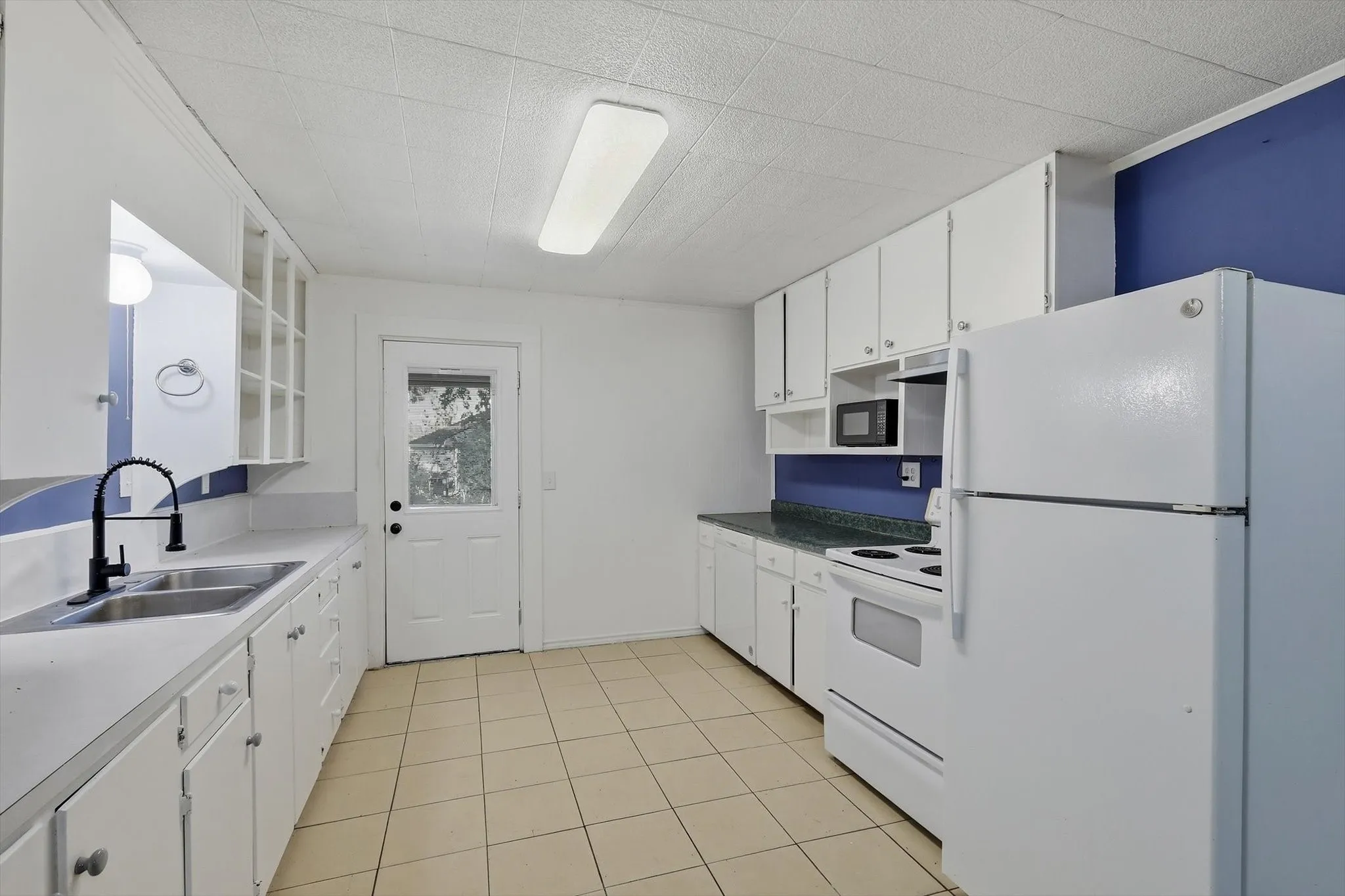 Kitchen featuring white cabinetry, dual basin stainless steel sink with a black gooseneck faucet, white appliances, and tiled flooring