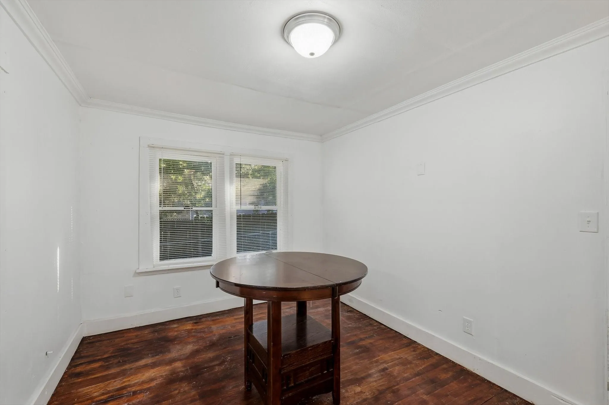 White walls, wood-finish flooring, two large windows, and crown molding