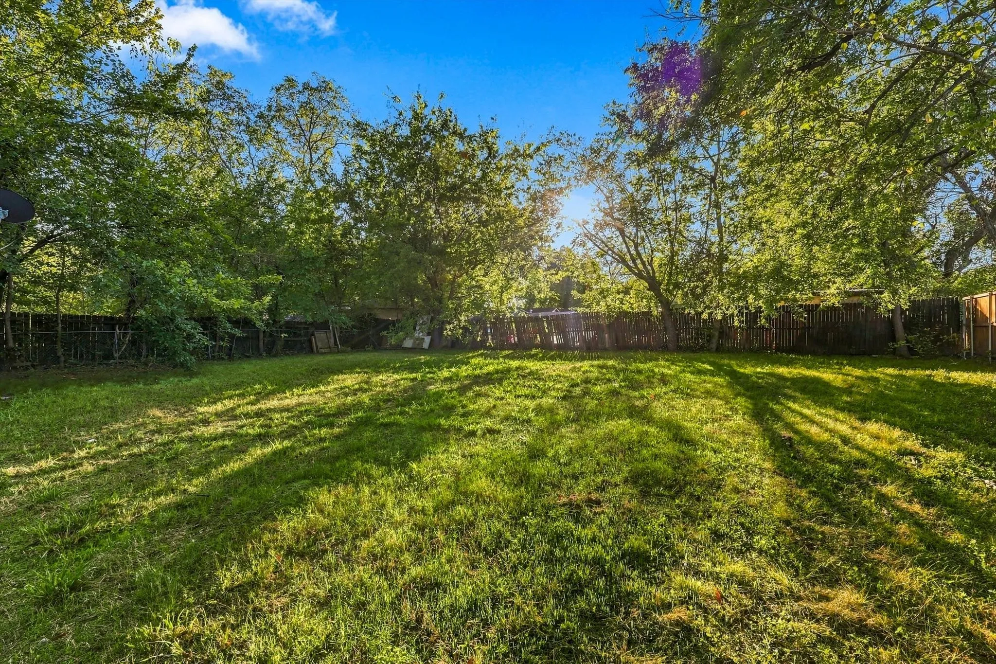 Expansive grass lawn bordered by mature trees and wood fencing