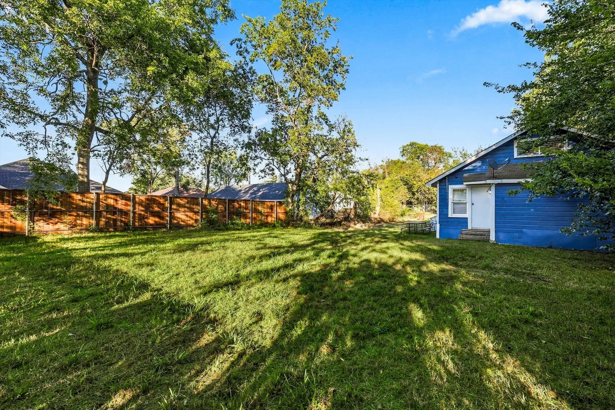 Expansive green lawn with mature trees and a wood-paneled privacy fence