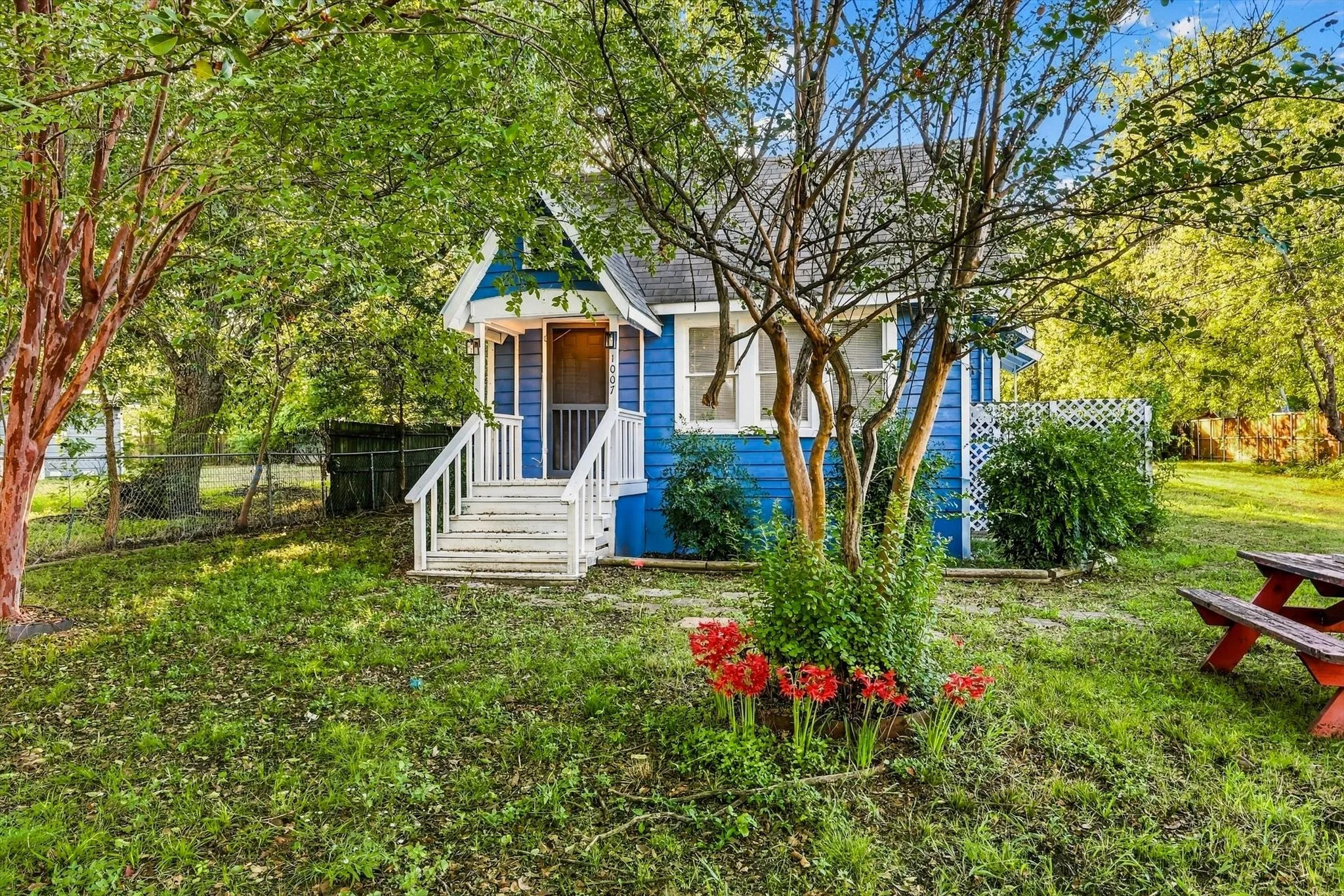 Blue exterior siding with white trim, white front porch railing, white porch steps, and mature trees