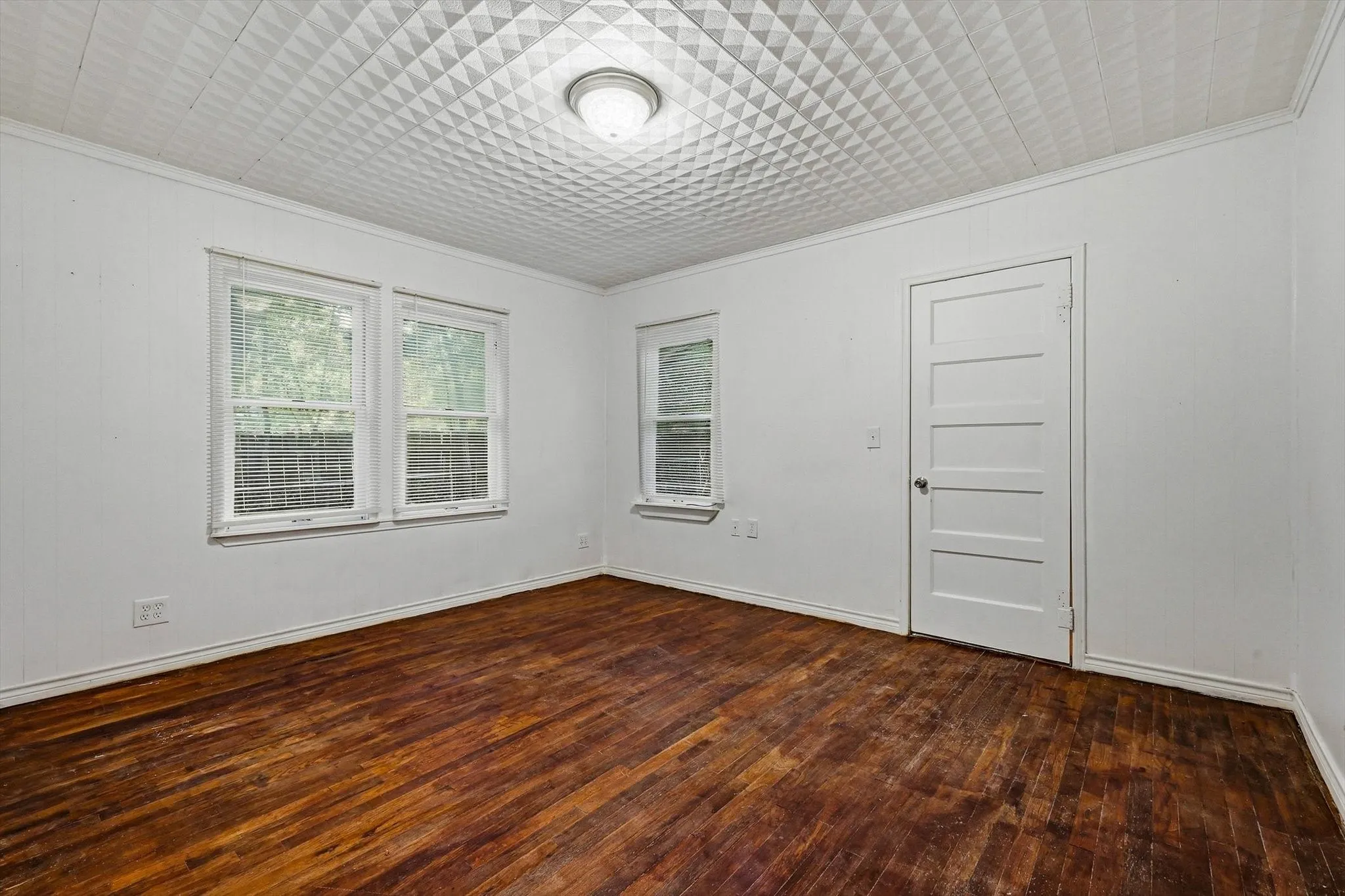 Wood-finish flooring, white walls, and a patterned ceiling with a flush-mount light fixture
