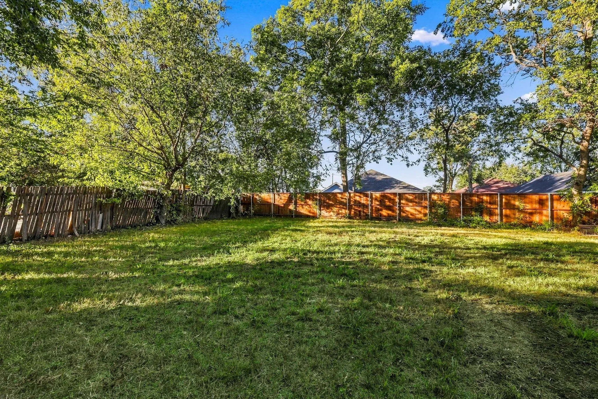 Expansive grassy yard with a wood privacy fence and mature trees
